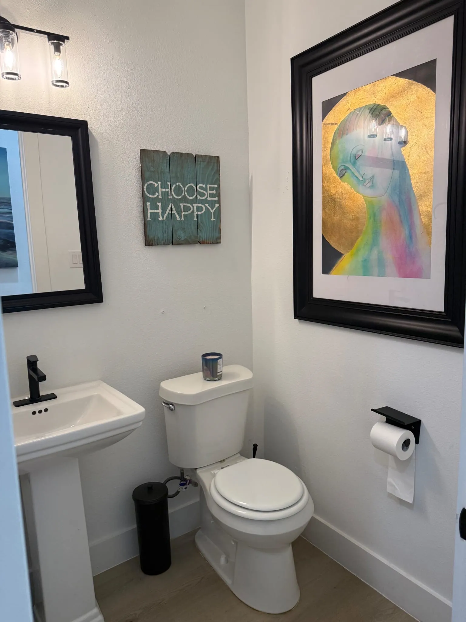 Pedestal sink with a matte black faucet, wall-mounted mirror, and wood-finish flooring