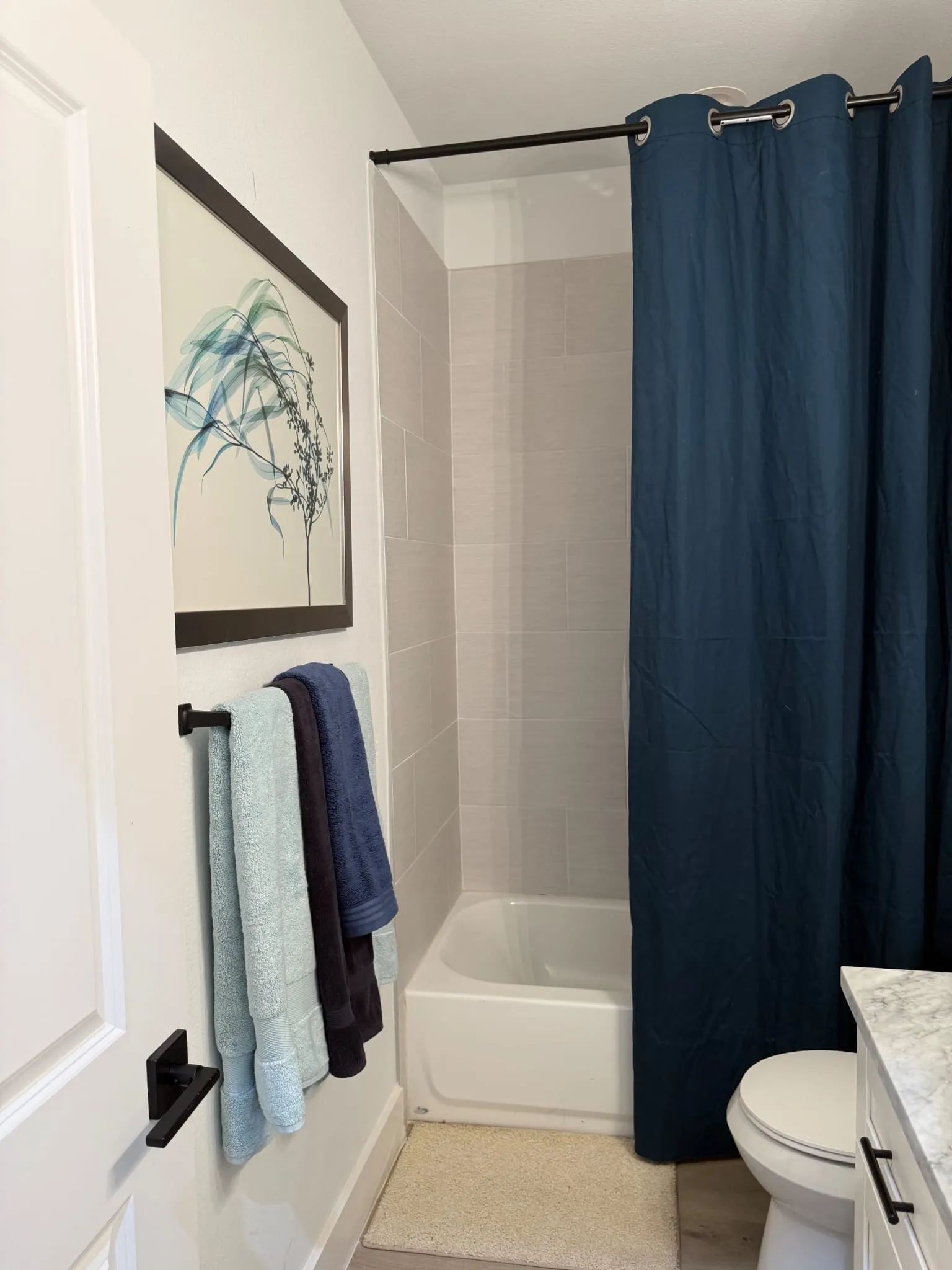 White porcelain bathtub with light gray subway tile surround and black shower rod