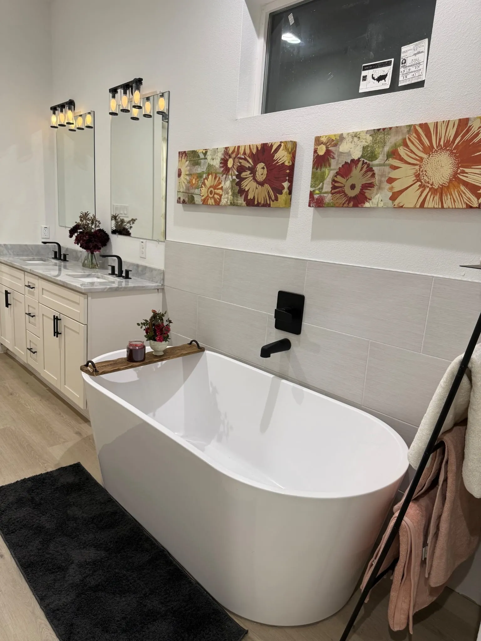 Freestanding soaking tub with a matte black wall-mounted faucet, dual vanity with quartz countertops, undermount sinks, and matte black fixtures, and wood-finish flooring
