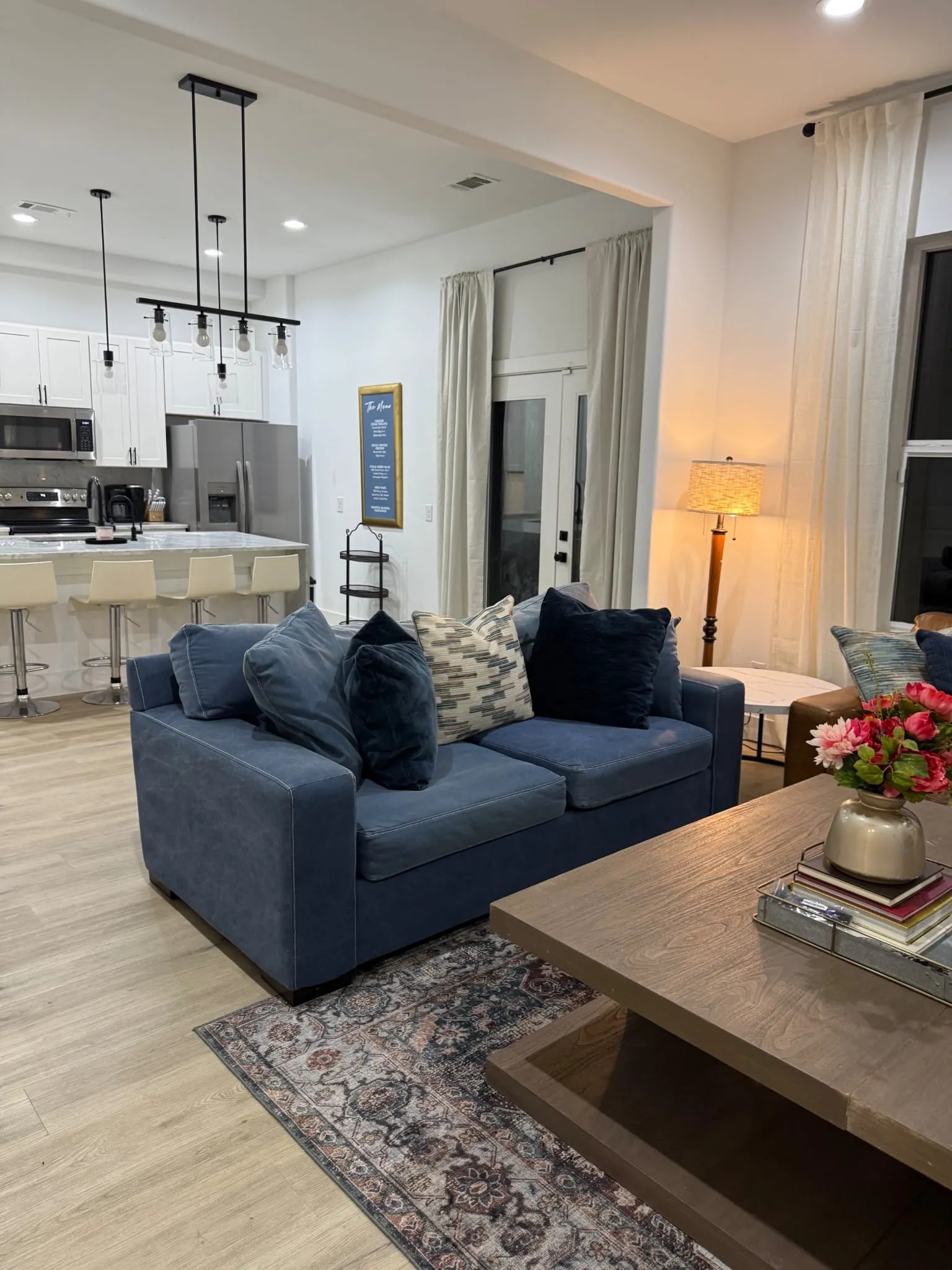 Open-concept living area with wood-finish flooring, white cabinetry, stainless steel appliances, and a kitchen island with seating