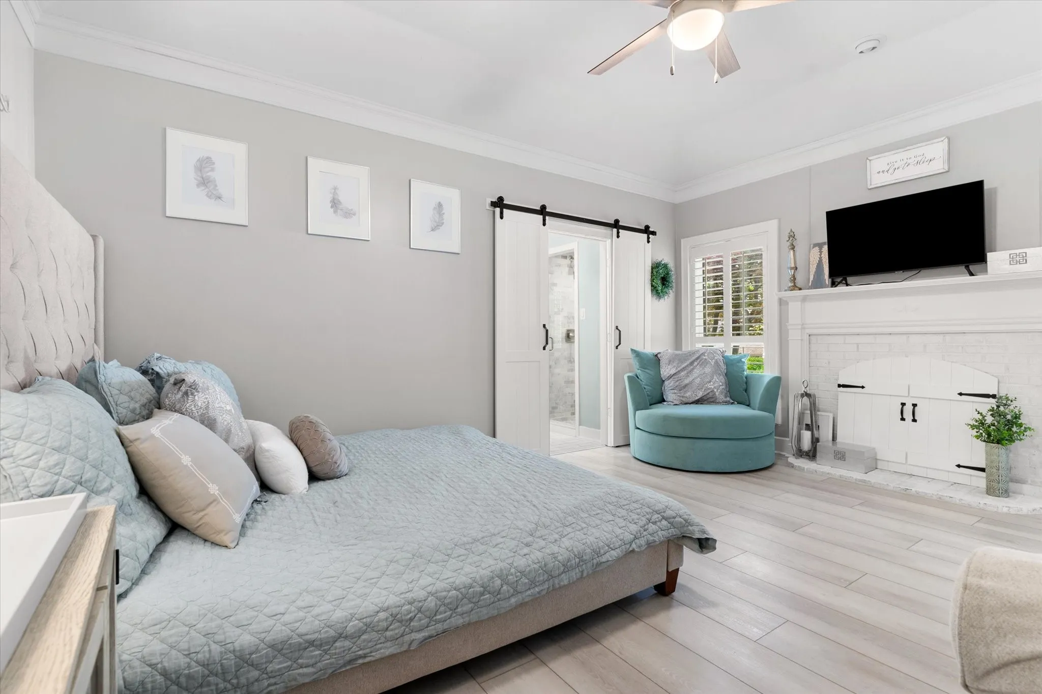 Vaulted ceiling with ceiling fan, light wood-finish flooring, white fireplace with decorative hearth, and sliding barn doors