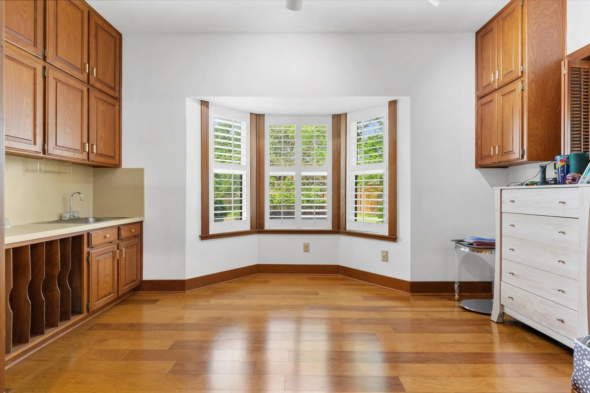 Hardwood flooring, bay window with plantation shutters, built-in cabinetry, integrated sink, and integrated shelving