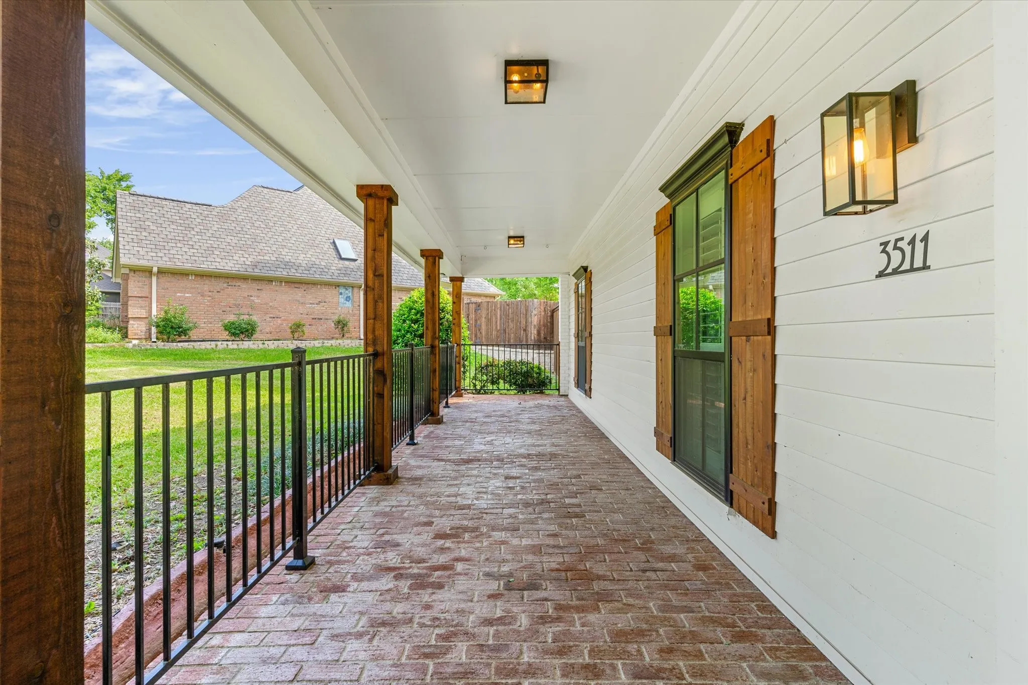 Covered porch with exposed brick flooring, wood-clad columns, and black metal railing