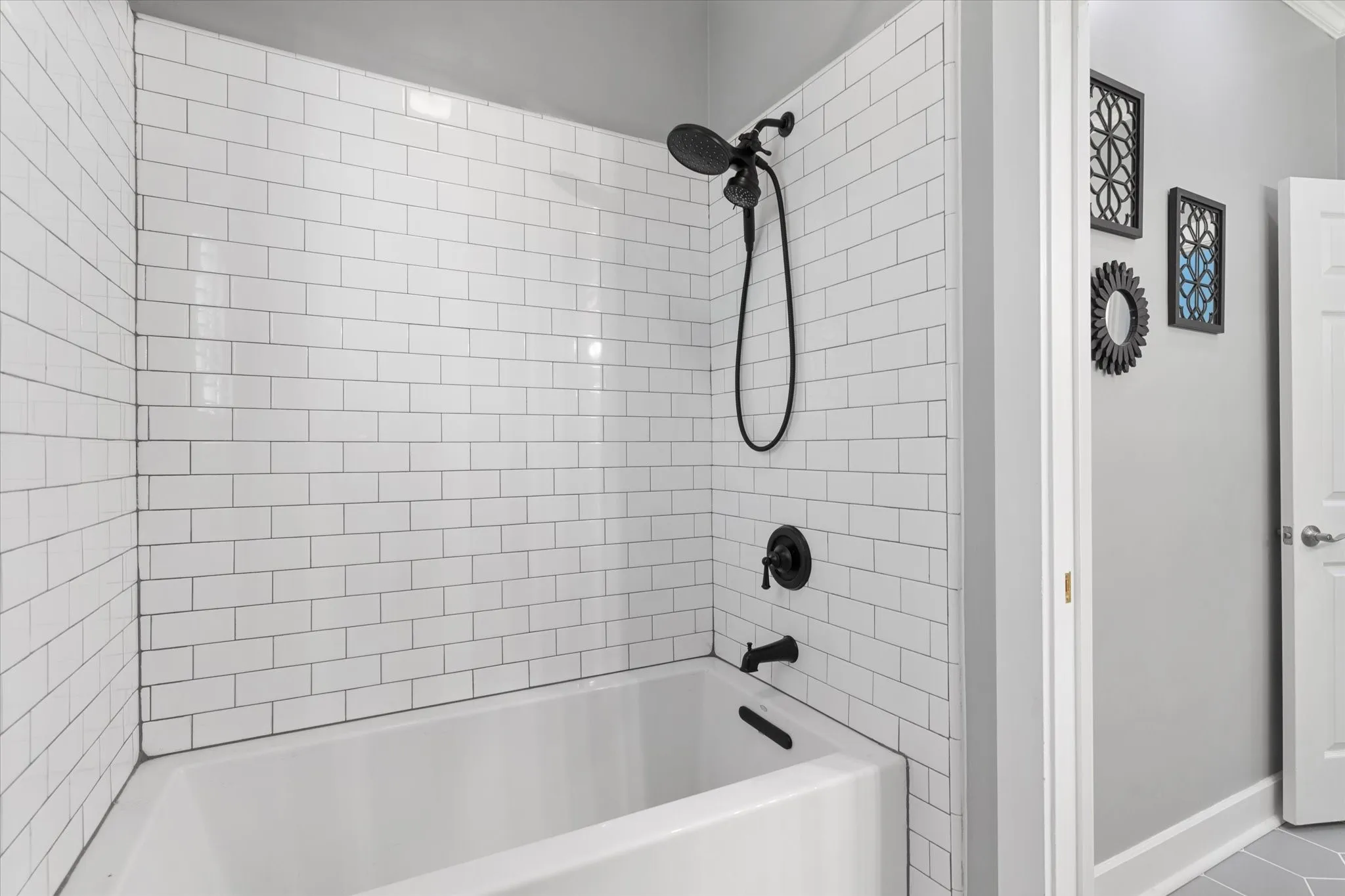 Bathtub with white subway tile surround, matte black shower fixtures, and a coordinating matte black faucet
