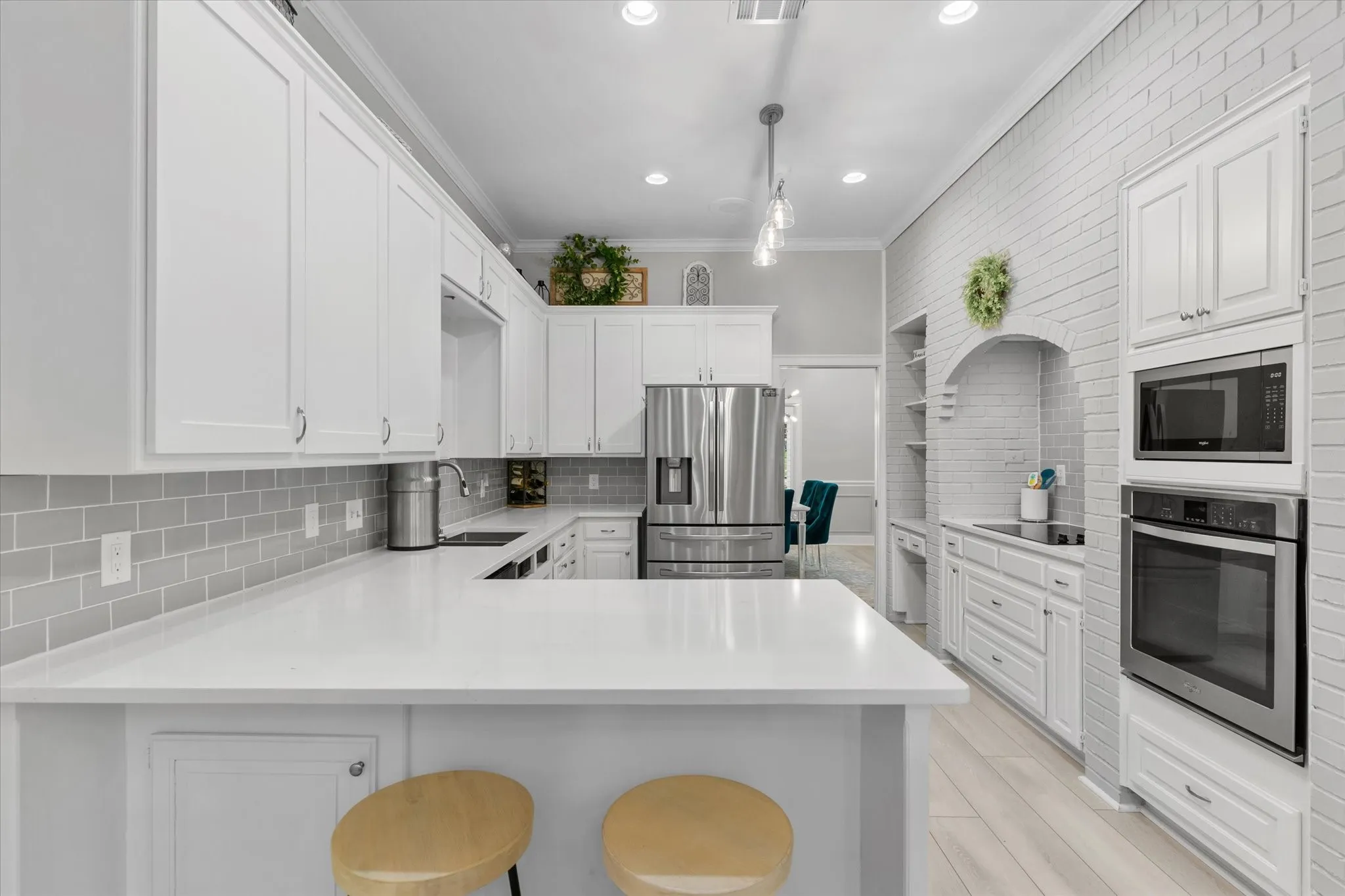 White shaker cabinetry, light-toned wood-finish flooring, stainless steel appliances, light gray subway tile backsplash, and recessed lighting