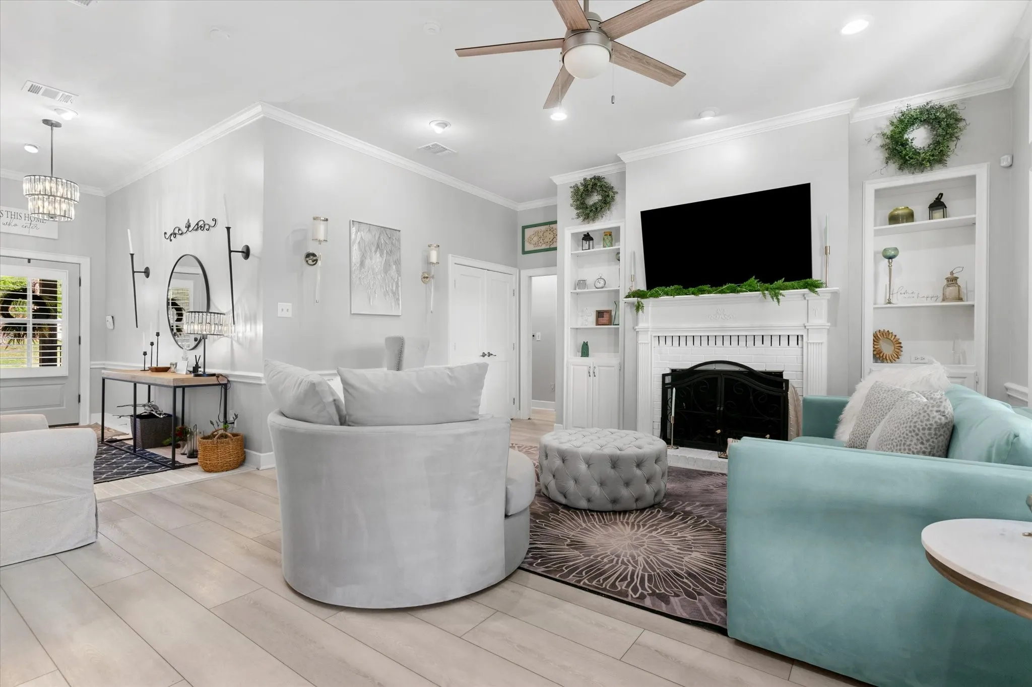 Light wood-finish flooring throughout, crown molding, built-in shelving, fireplace with mantel, and ceiling fan with integrated lighting