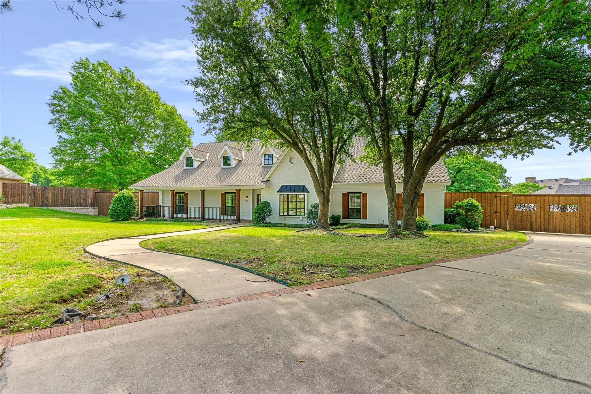White exterior with a covered front porch, dark shutters, dormer windows, and a concrete driveway