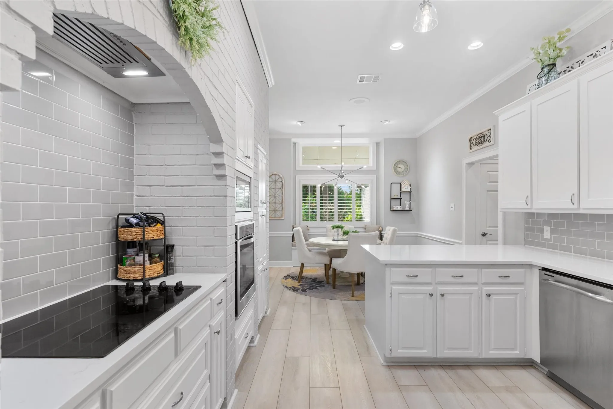 White shaker cabinetry, light wood-finish flooring, undermount sink, built-in stainless steel appliances, and subway tile backsplash