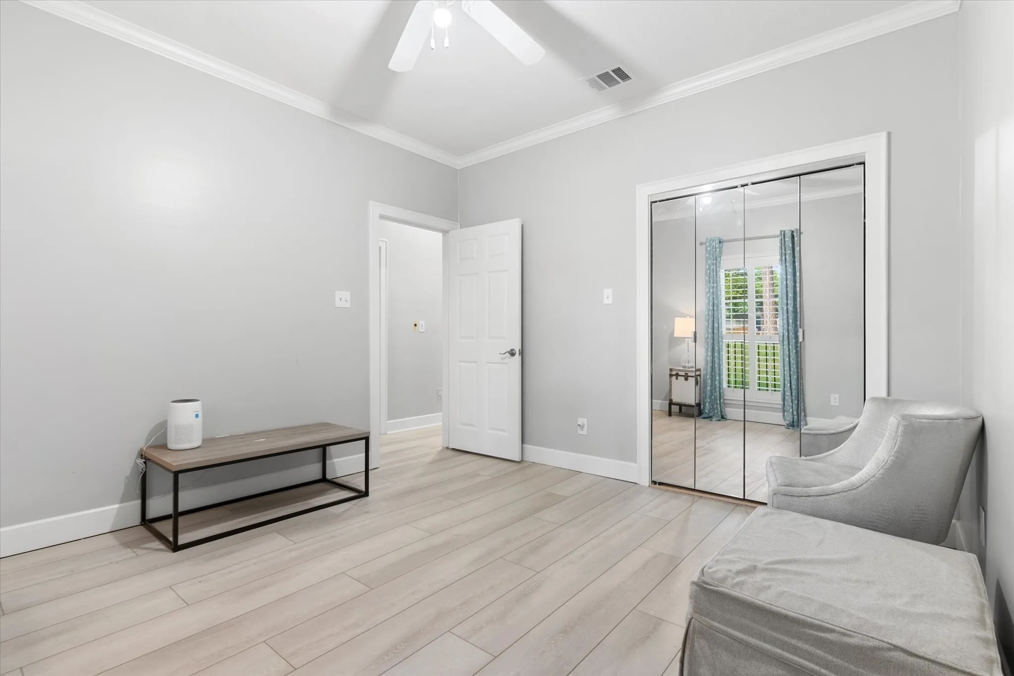 Light wood-finish flooring, ceiling fan, crown molding, and mirrored closet doors