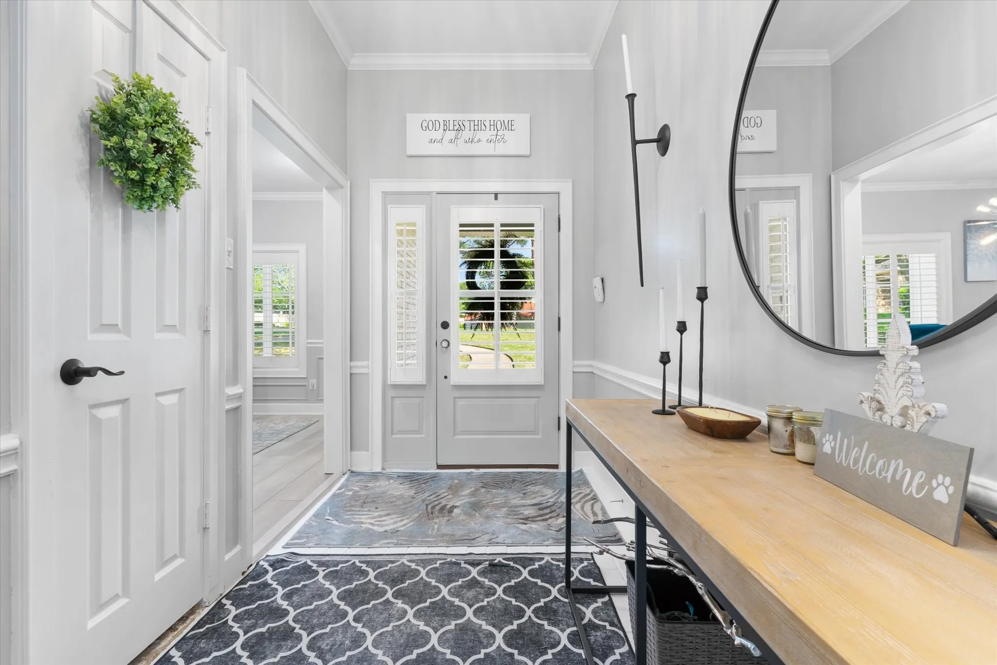 Double entry doors with sidelights, featuring interior plantation shutters, a round wall-mounted mirror, and a console table