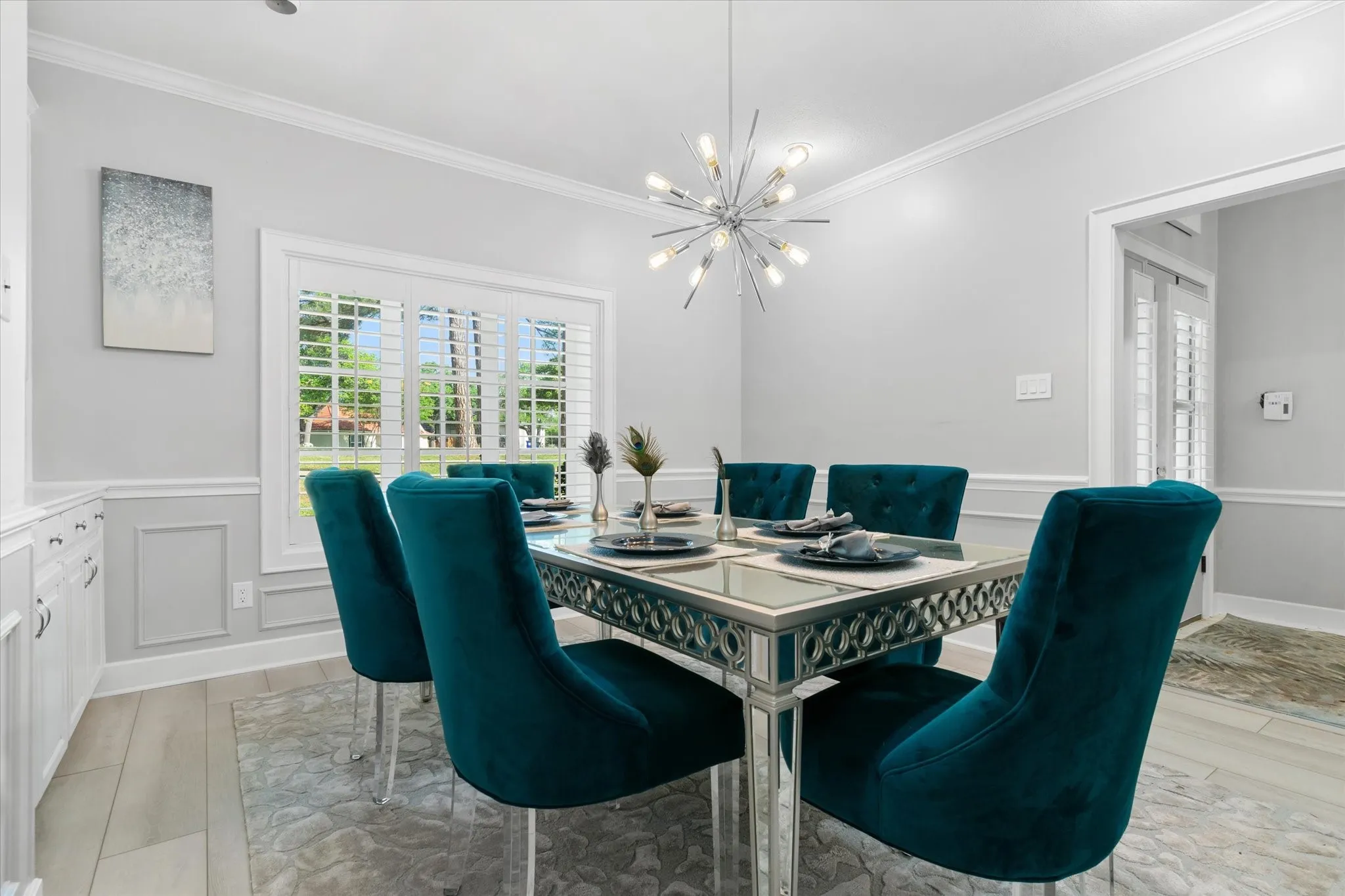 Recessed lighting with a contemporary chandelier, crown molding, chair rail with panel molding, and plantation shutters