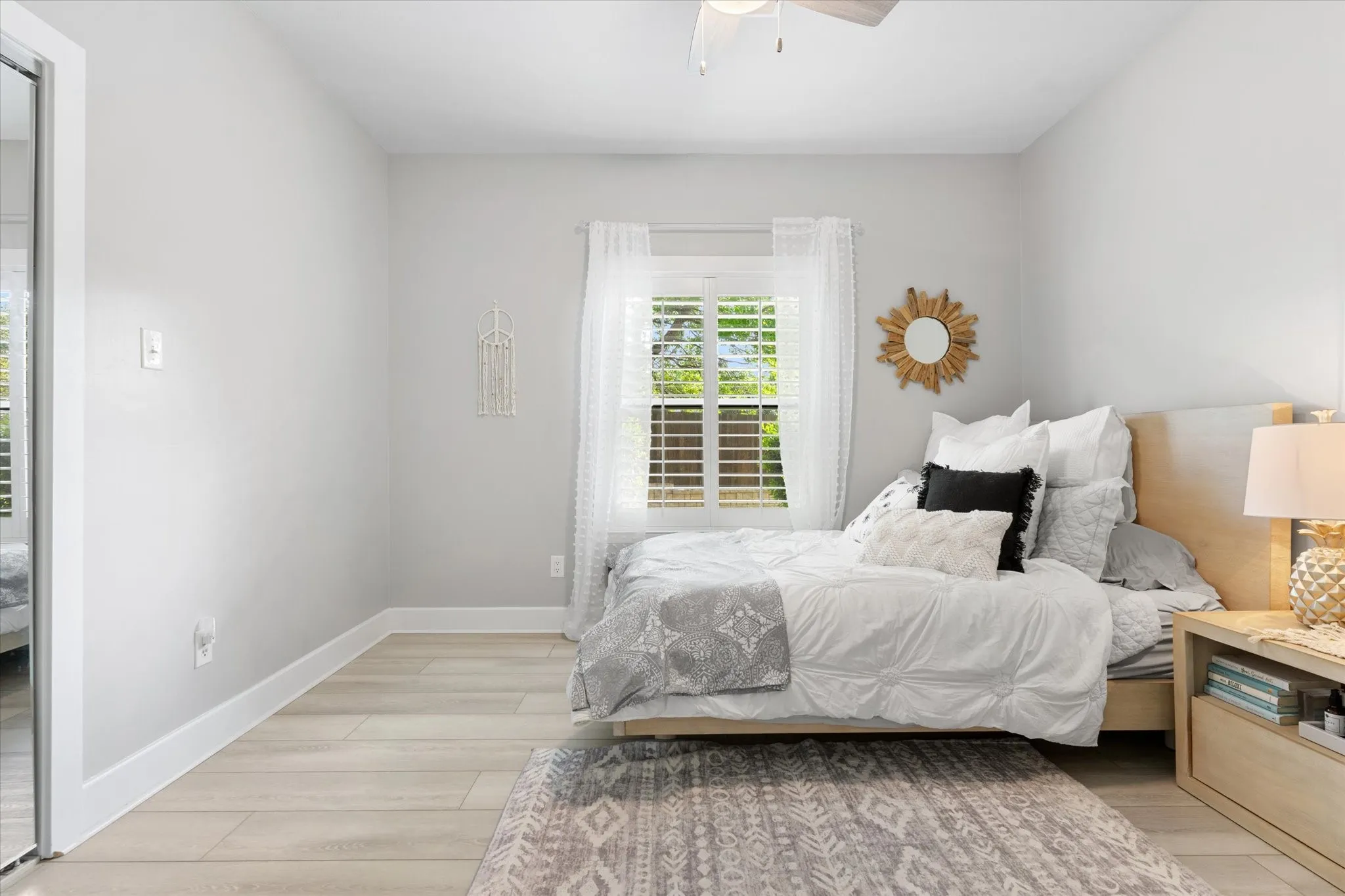 Wood-finish flooring, white plantation shutters, ceiling fan, and sliding mirrored closet doors