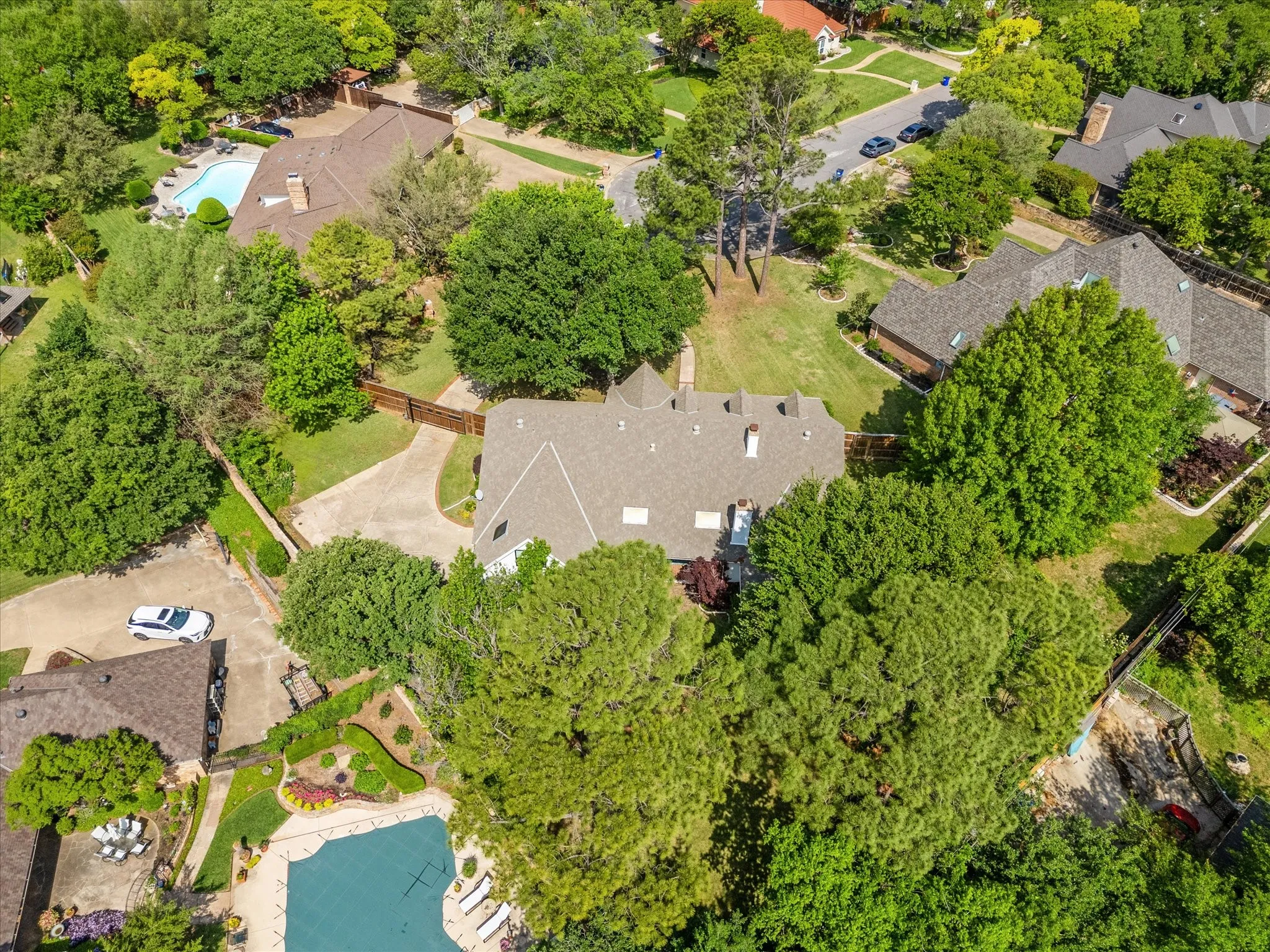Aerial perspective highlighting a residential property with a shingle roof, mature landscaping, and a concrete driveway