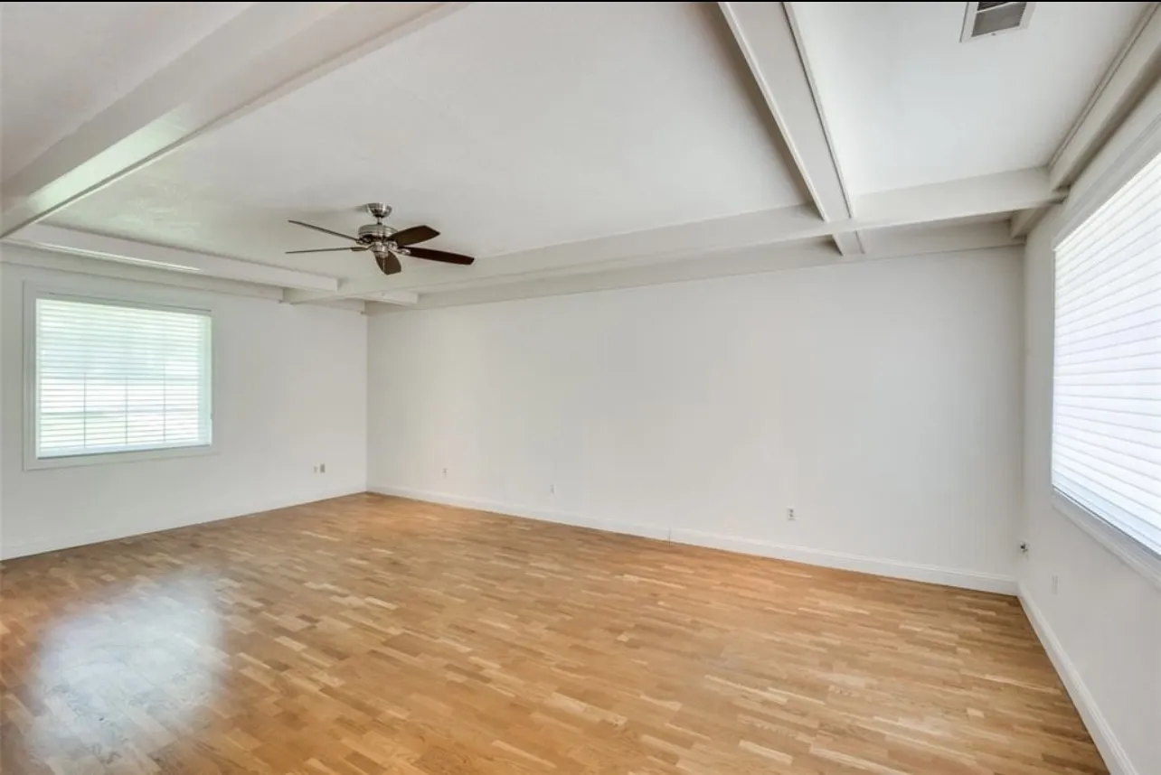 Spacious room featuring wood-finish flooring, white walls, and a coffered ceiling with a ceiling fan