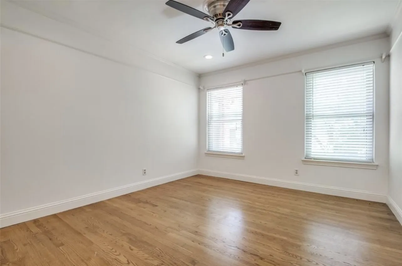 Wood-finish flooring with white baseboards, crown molding, and two windows with blinds