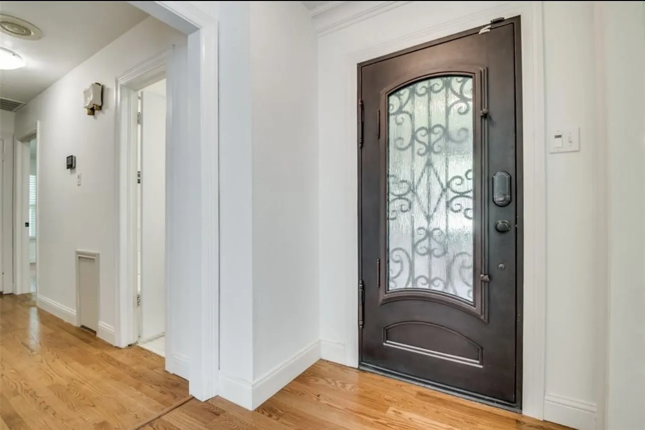 Wrought iron entry door with an arched glass insert, wood-finish flooring, and white painted walls