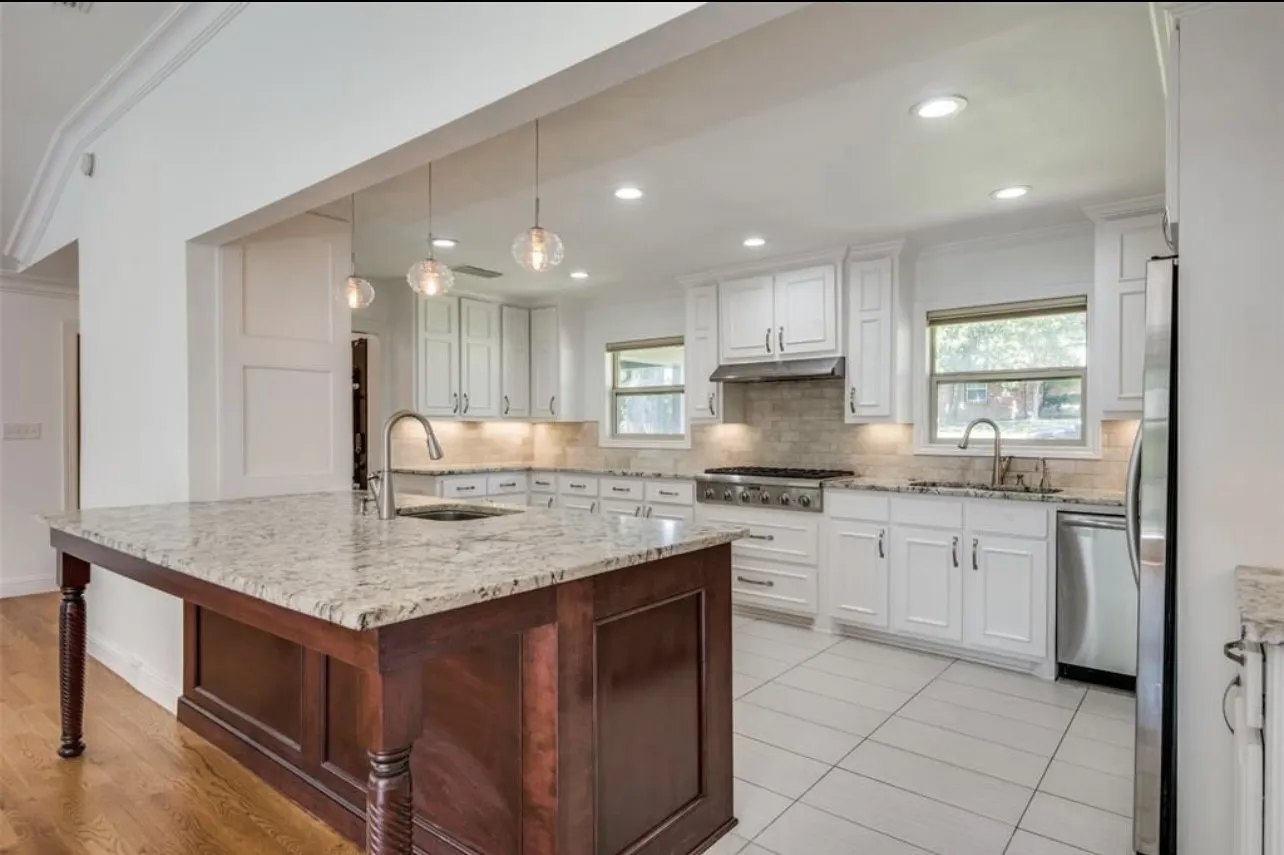 Gourmet kitchen featuring a large central island with an undermount sink, granite countertops, stainless steel appliances, and white cabinetry