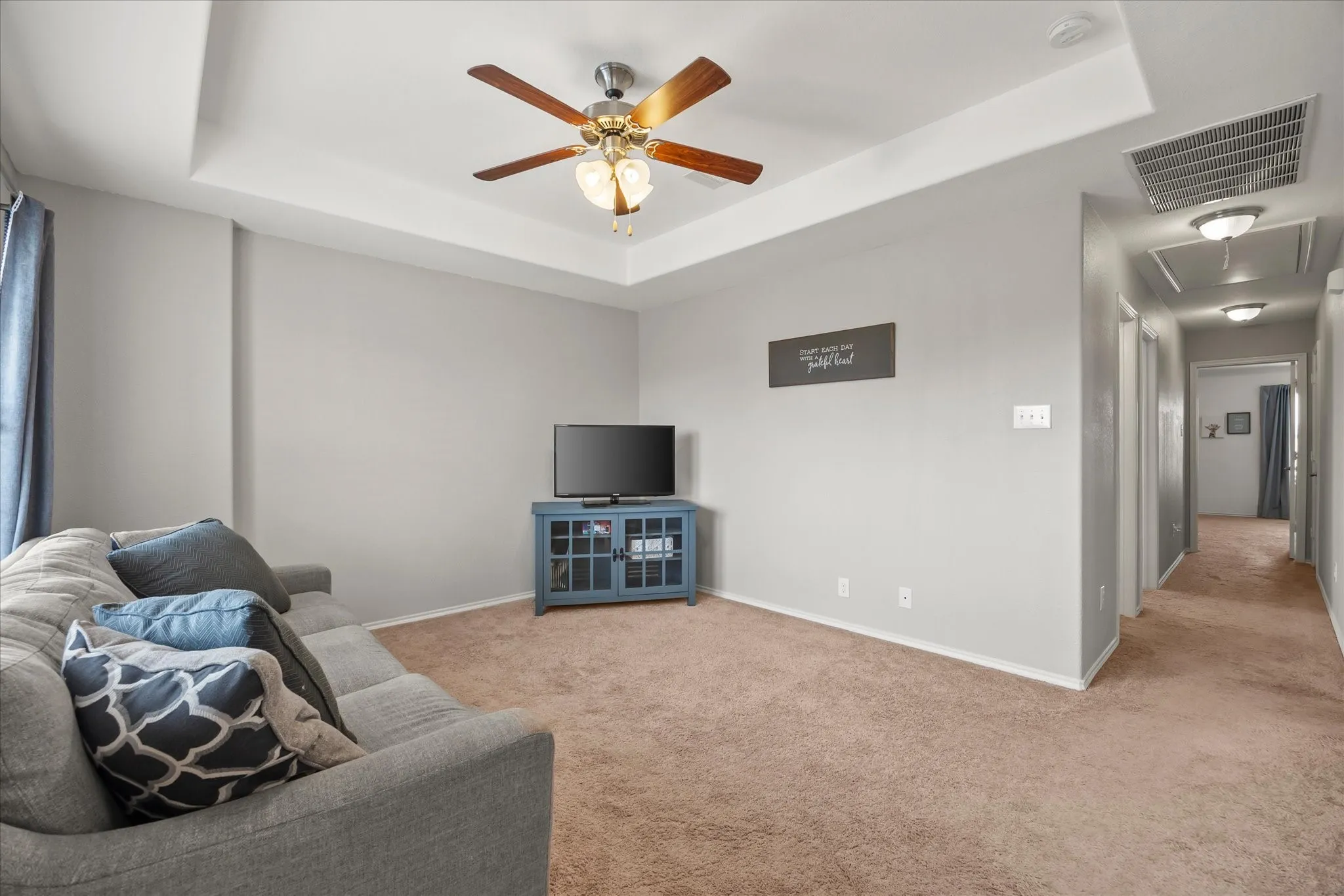 Tray ceiling with a ceiling fan, light gray wall paint, and brown carpeting
