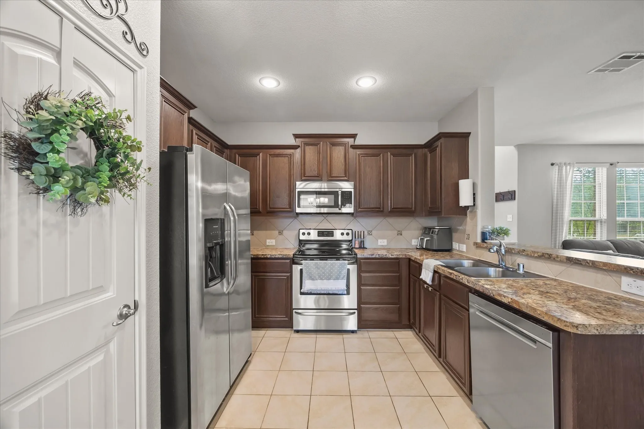 U-shaped kitchen with wood-finish cabinetry, tile flooring, stainless steel appliances, and a double basin sink