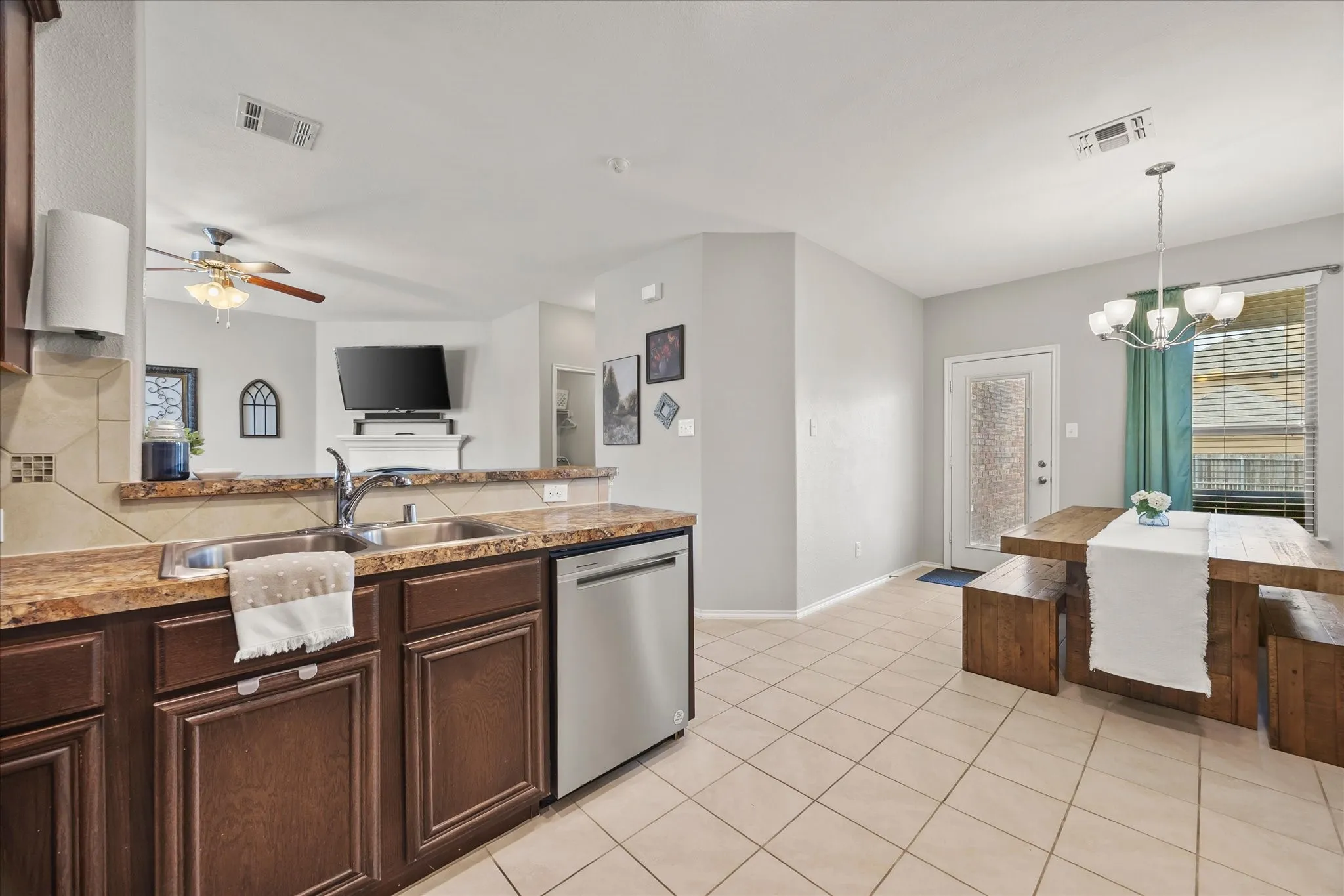 Open-concept kitchen and dining area featuring a tile backsplash, stainless steel dishwasher, double basin sink, and a multi-light chandelier