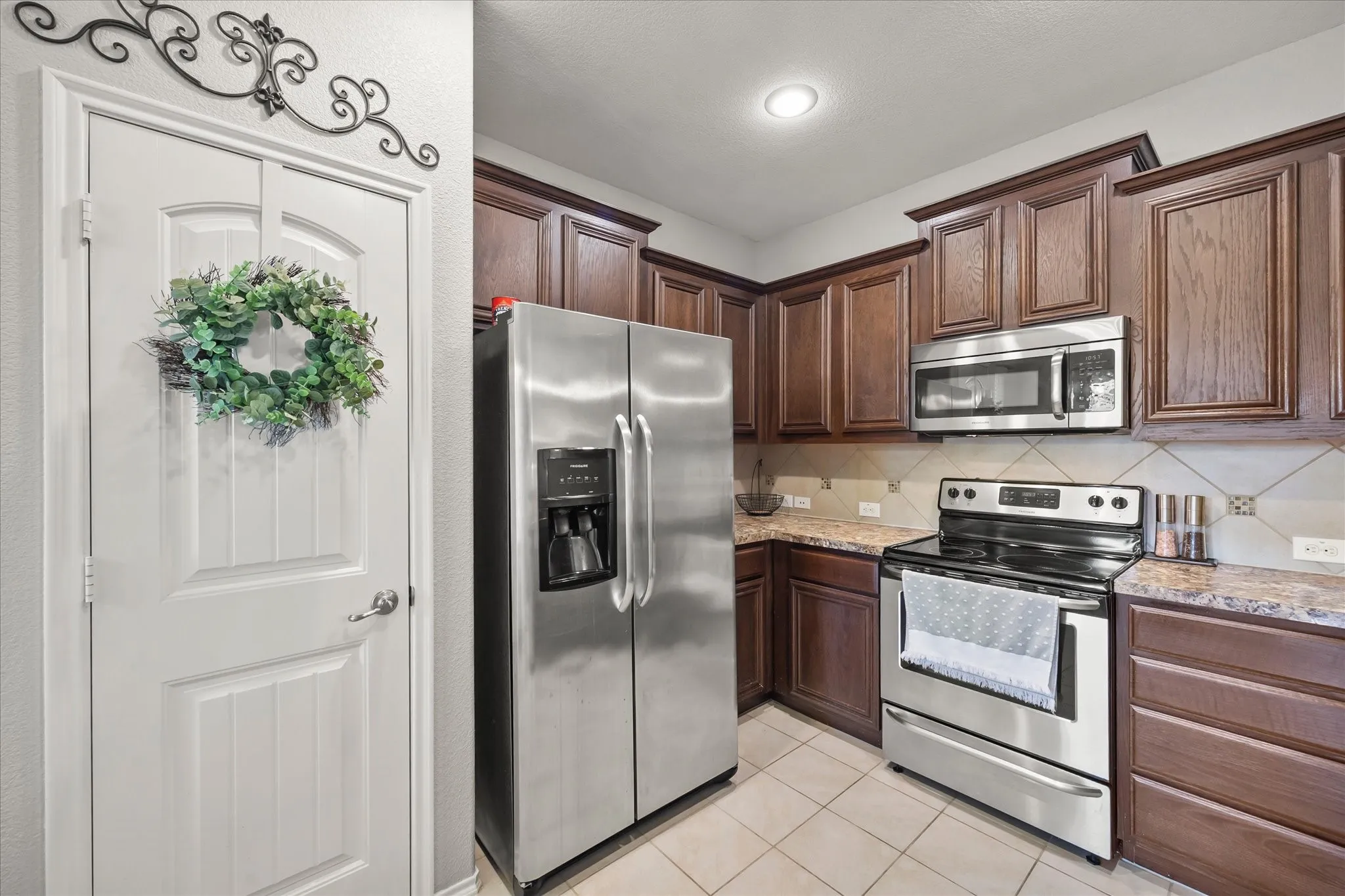 Kitchen featuring wood cabinetry, stainless steel appliances, tile flooring, and a tile backsplash