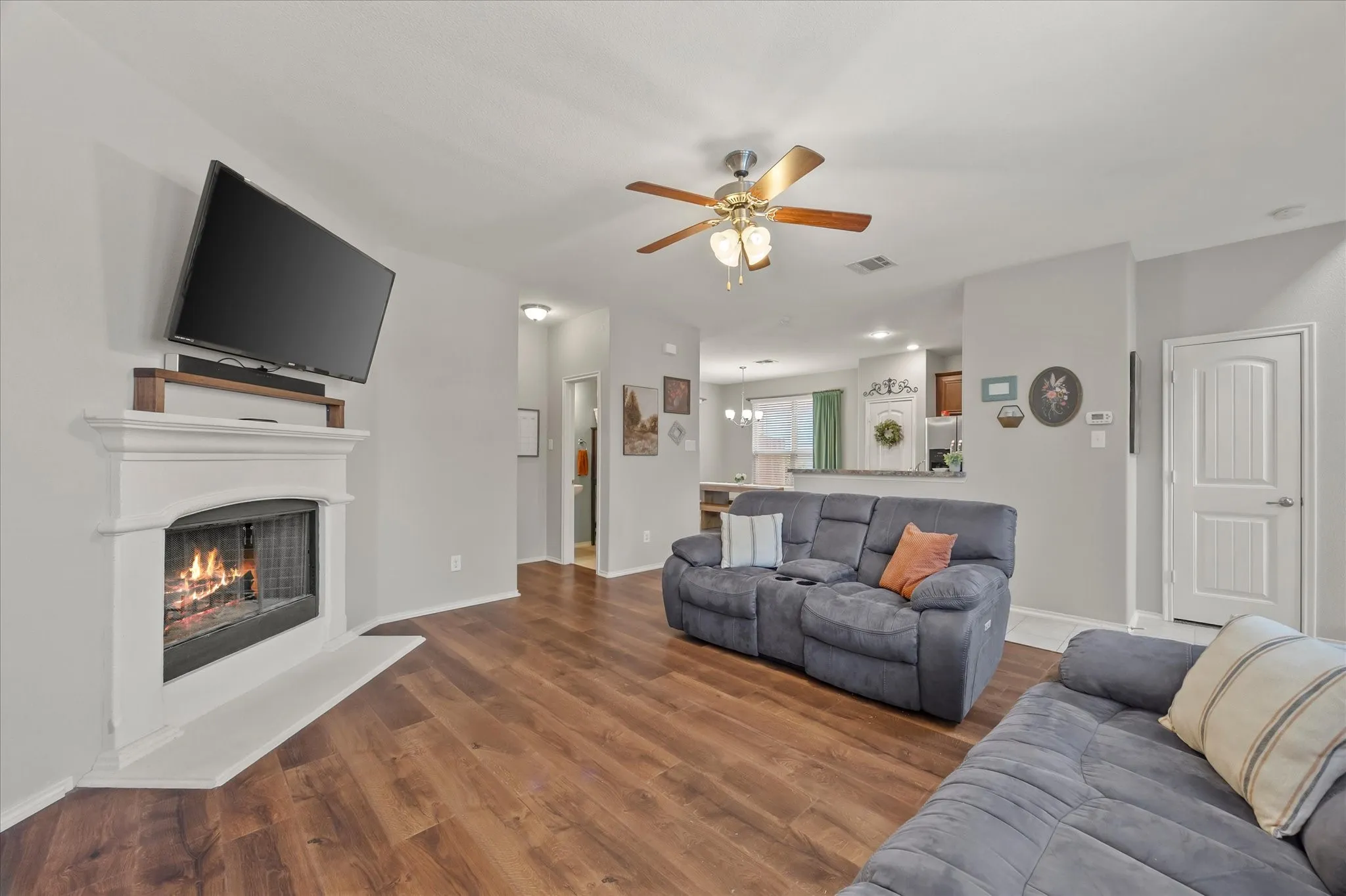 Living area with wood-finish flooring, a white mantel fireplace, and a ceiling fan with integrated lighting