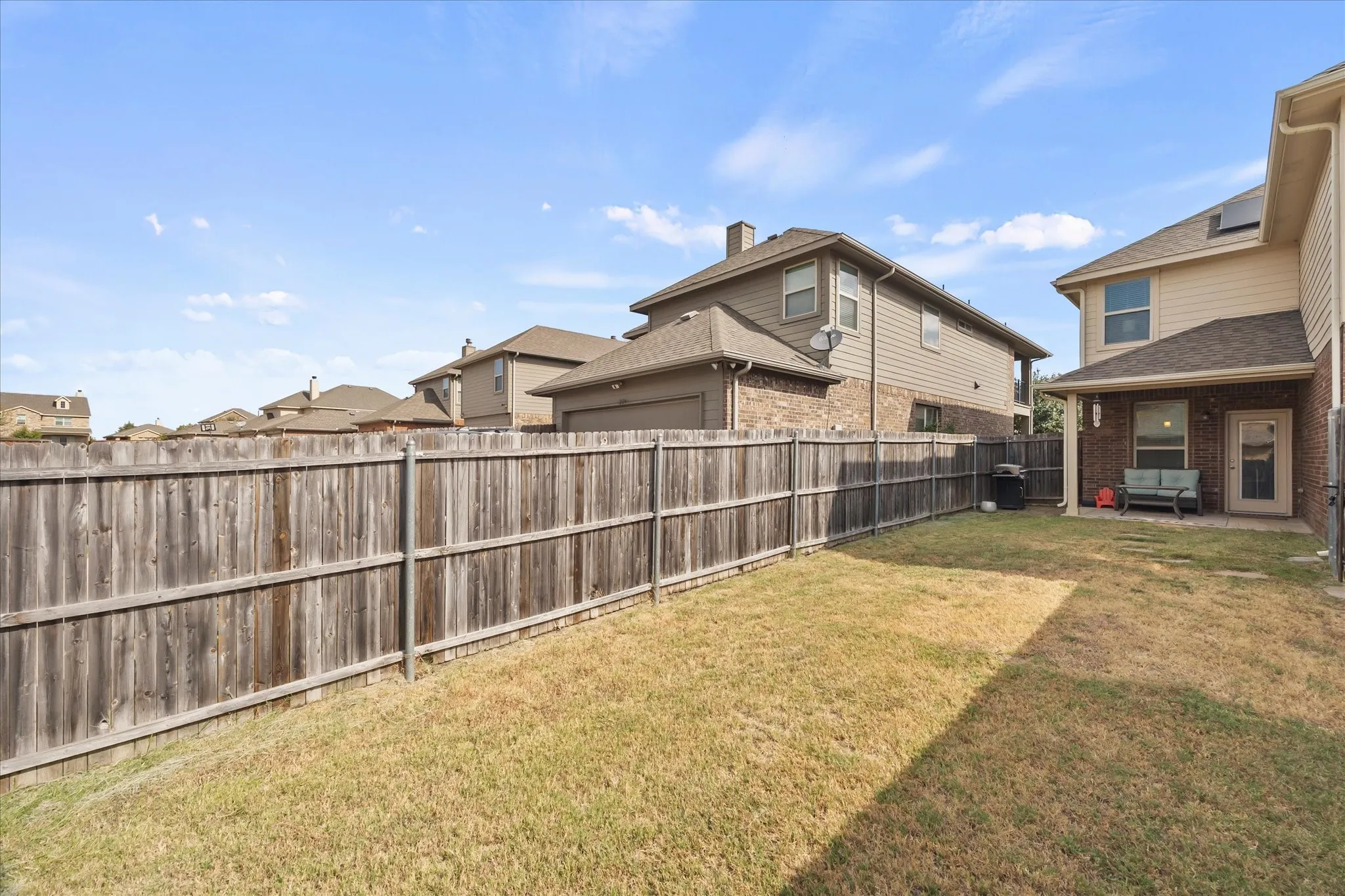 Fenced backyard with a covered patio, brick and siding exterior, and a glass-paneled back door