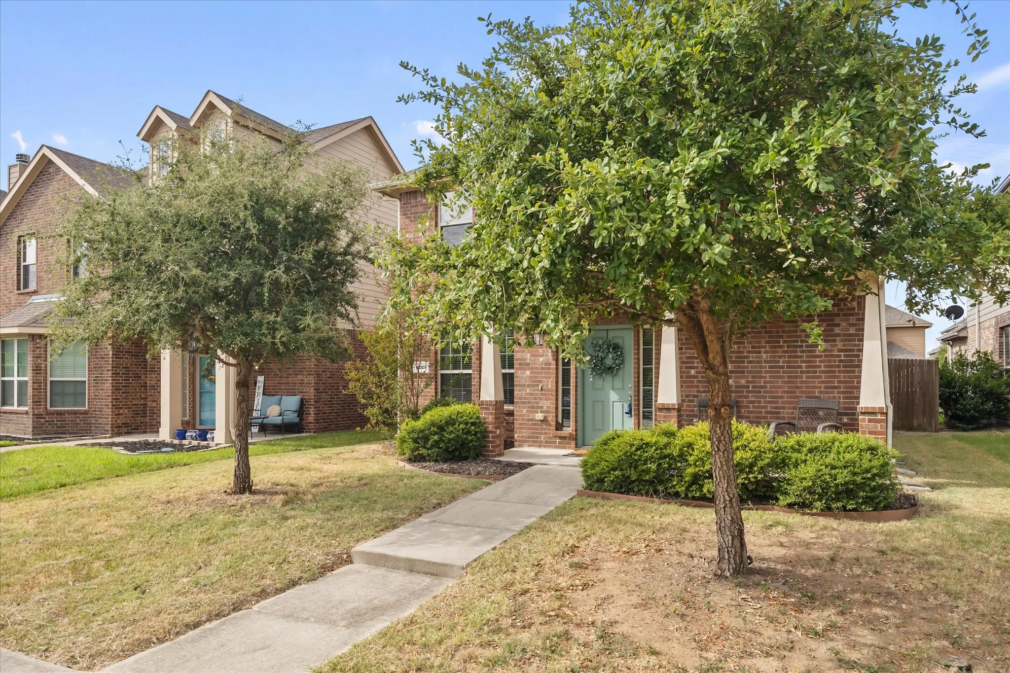Brick exterior, light blue entry door, concrete pathway, mature trees, manicured shrubs