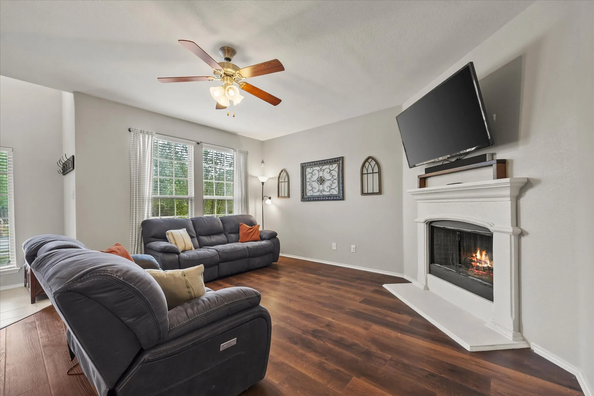 Living area featuring wood-finish flooring, a white mantel fireplace, and multiple windows