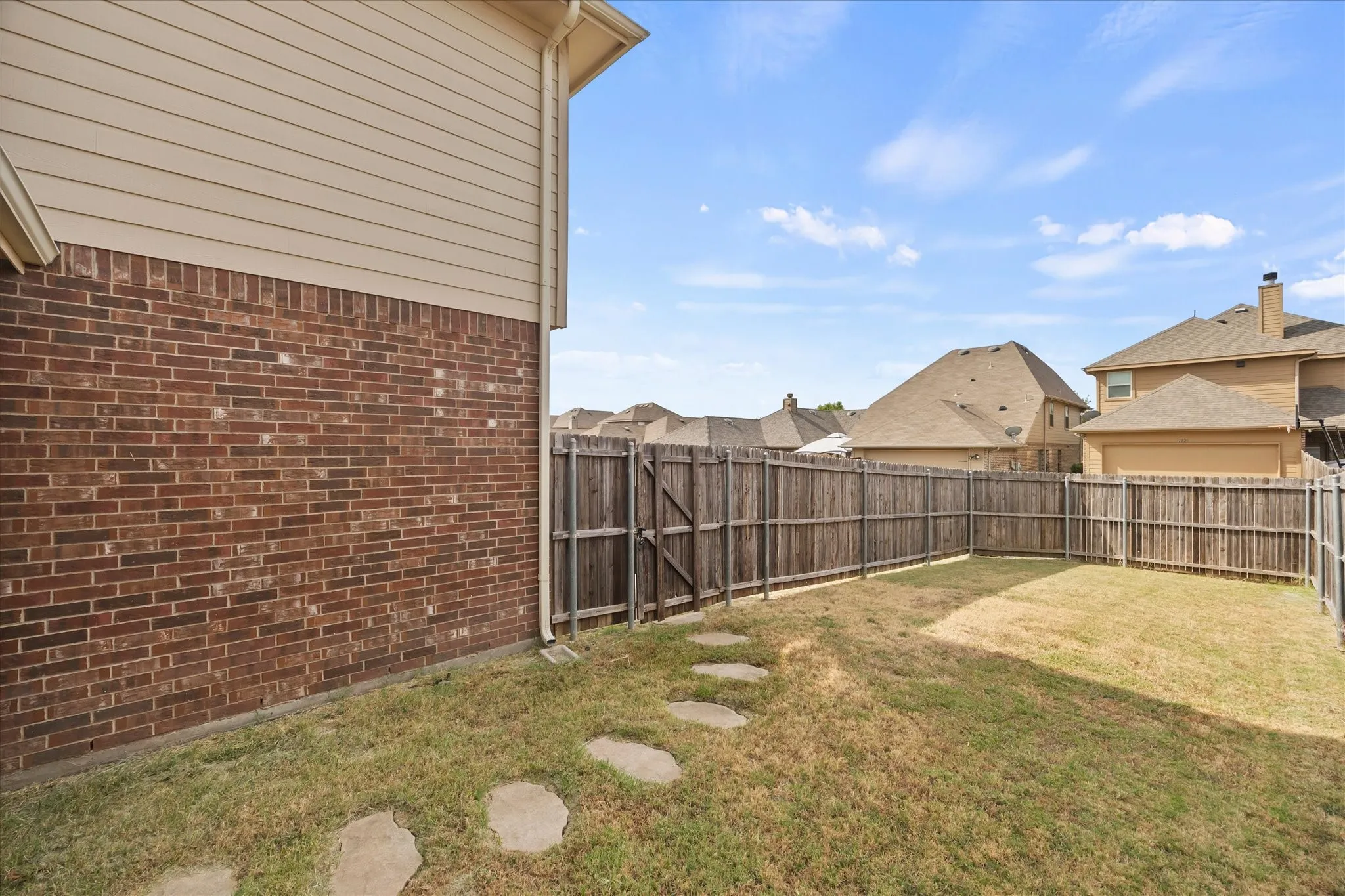 Expansive fenced backyard featuring a stone paver pathway and a brick and siding exterior