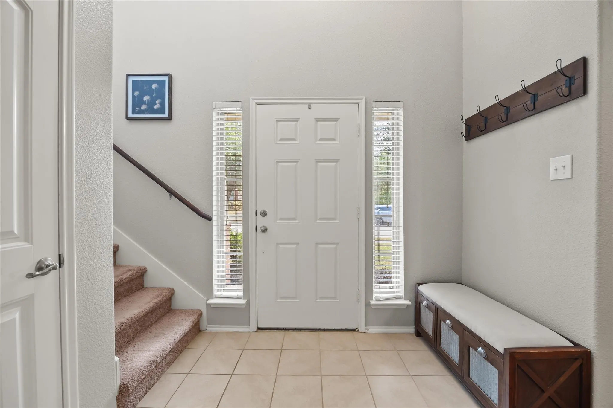 Foyer featuring a paneled entry door, side light windows with blinds, tiled flooring, and a carpeted staircase with a wood handrail
