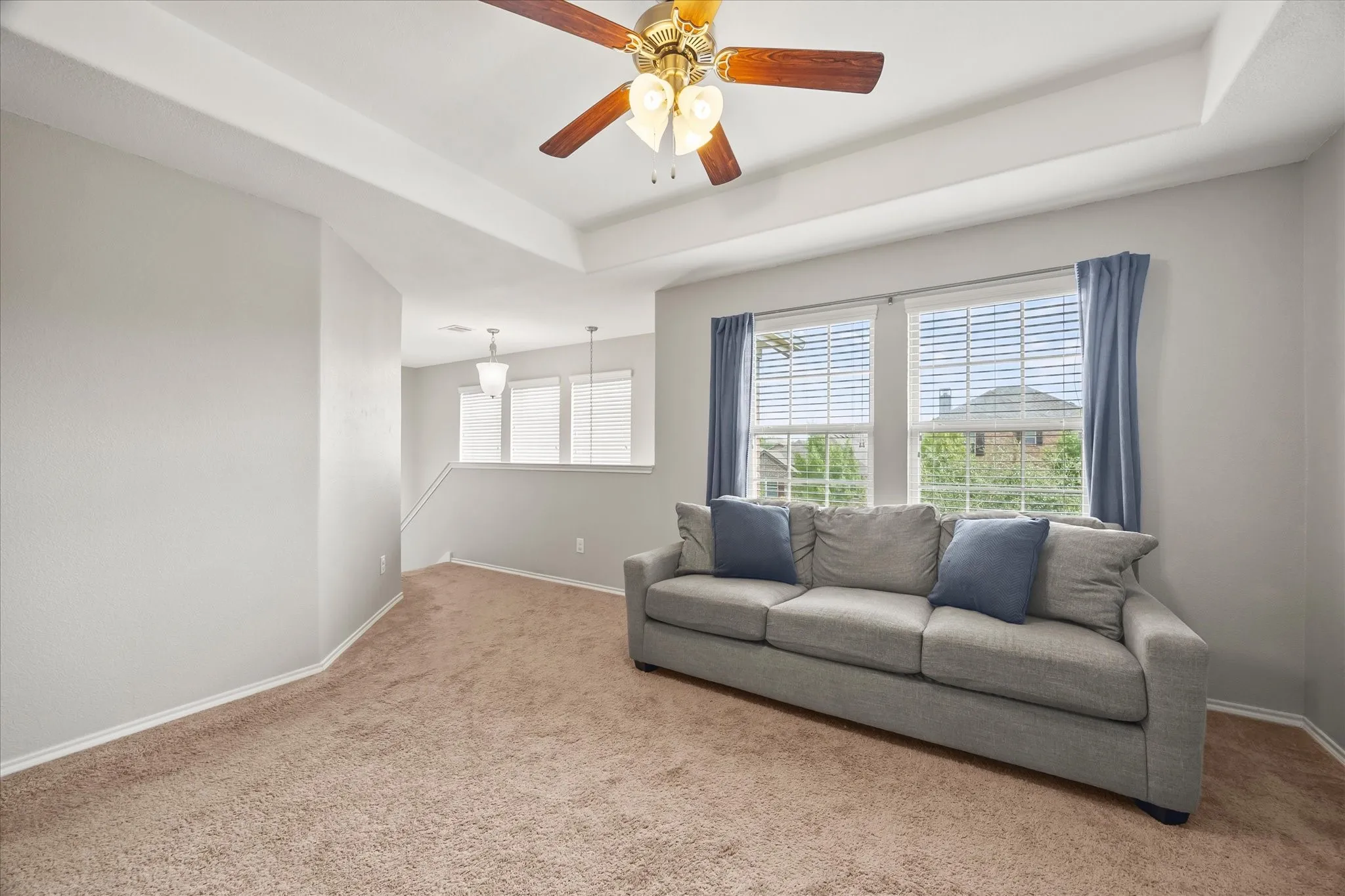 Tray ceiling with a ceiling fan, carpeted flooring, and multiple windows with blinds