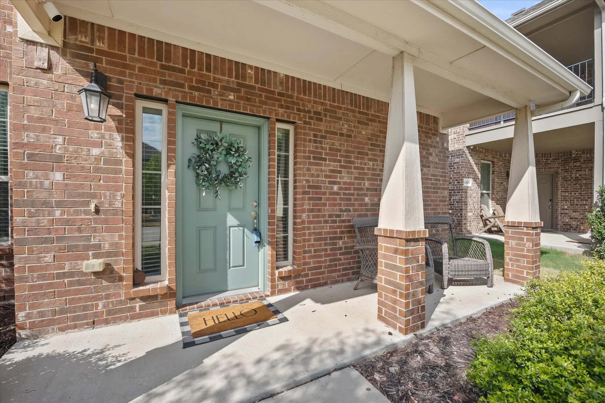 Brick exterior with a covered porch, featuring a panel-style front door, two sidelight windows, and an exterior wall lantern