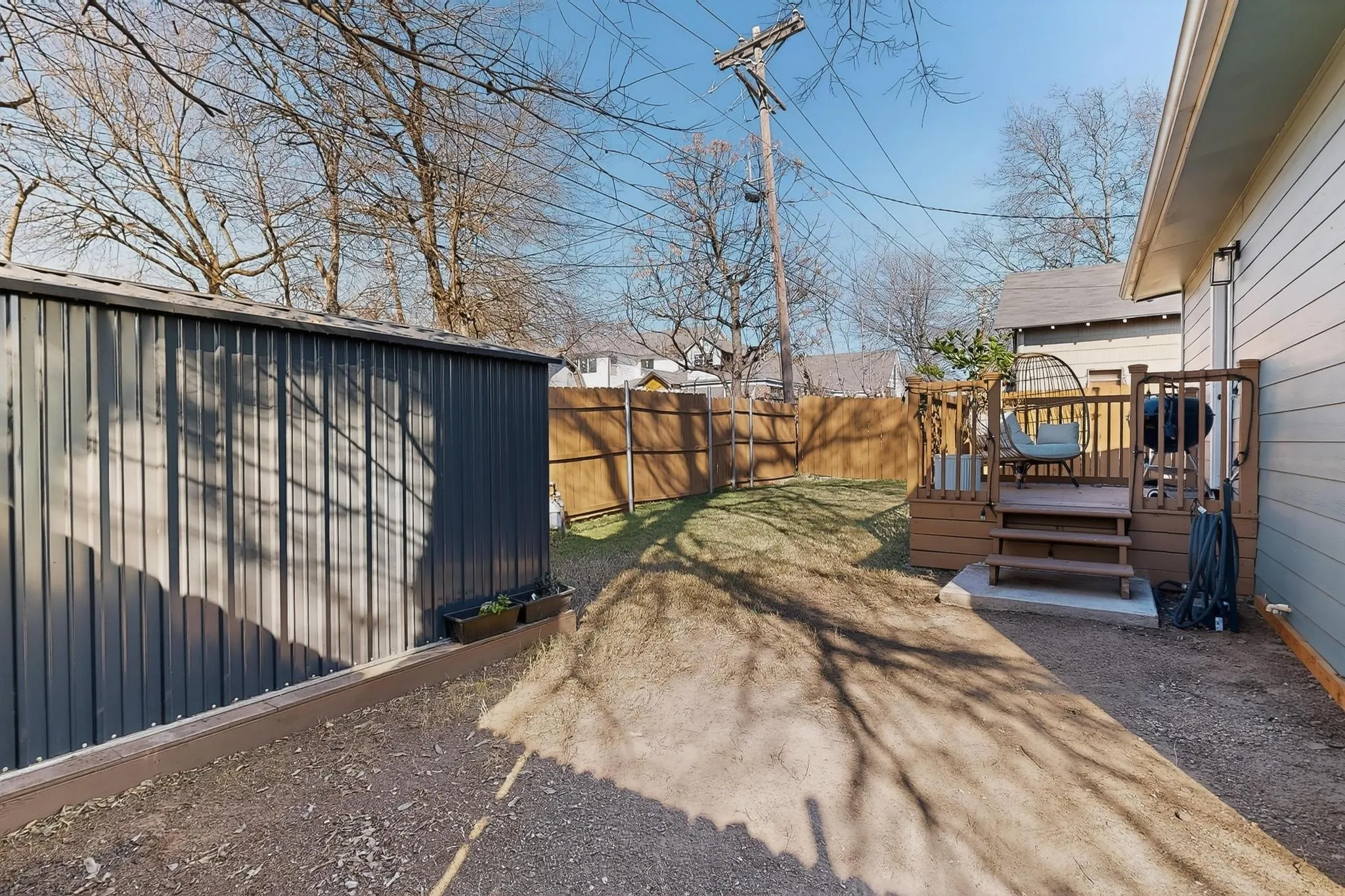 Backyard featuring a wood-toned deck with railing and stairs, a privacy fence, and a corrugated metal shed