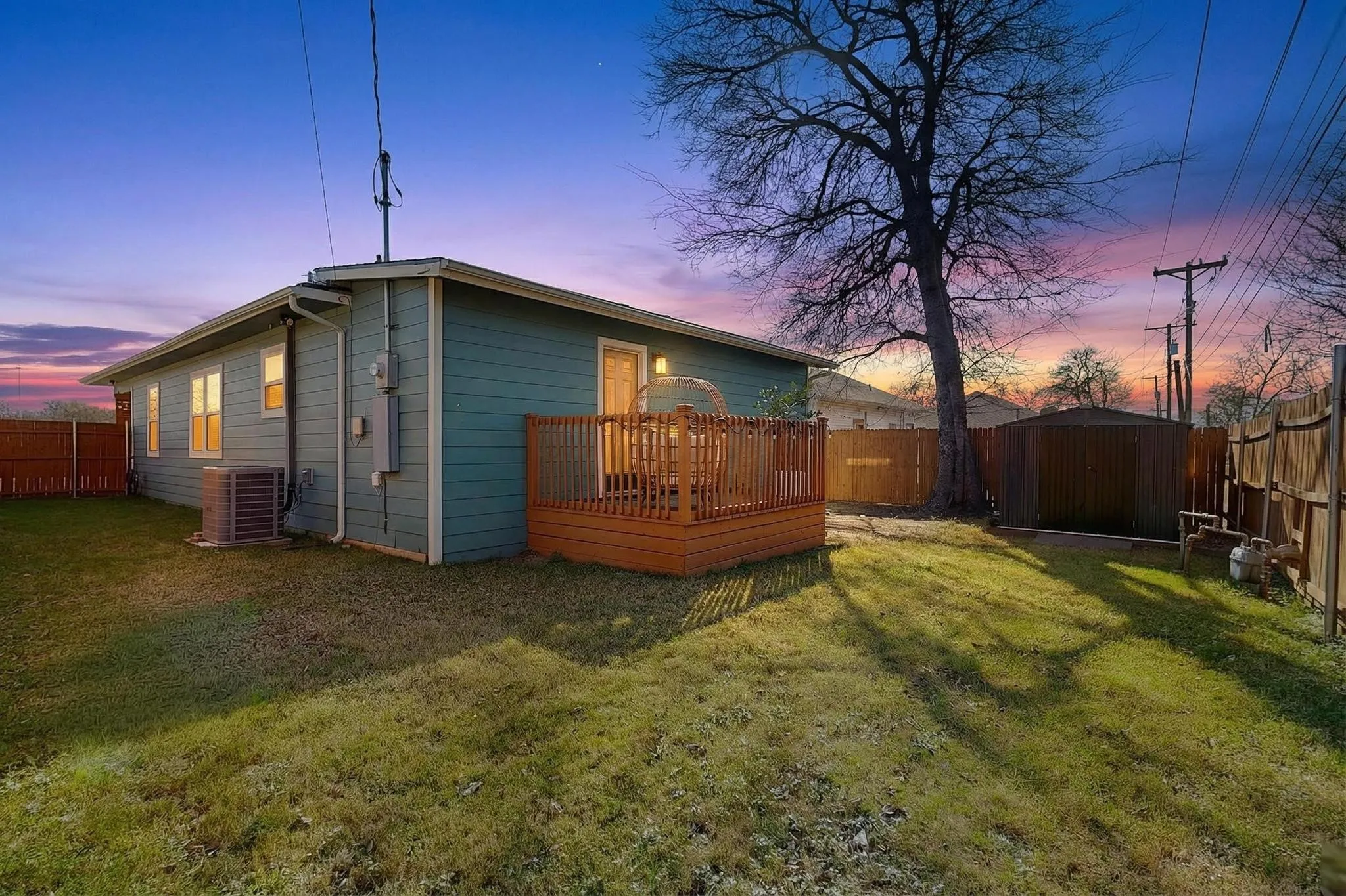 Rear exterior with teal siding, a built-in wood deck, and a detached storage shed