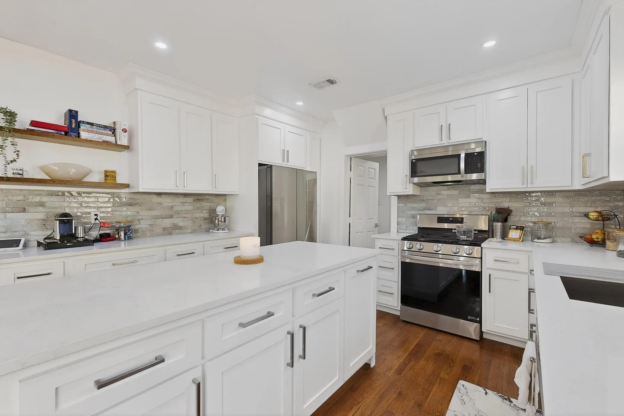 Kitchen featuring white cabinetry, light-toned backsplash, stainless steel appliances, a center island, and wood-finish flooring