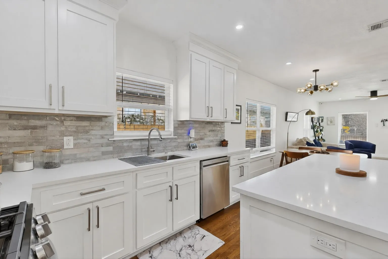 White cabinetry with brushed nickel hardware, stainless steel sink, integrated dishwasher, light-toned stone backsplash, and white countertops