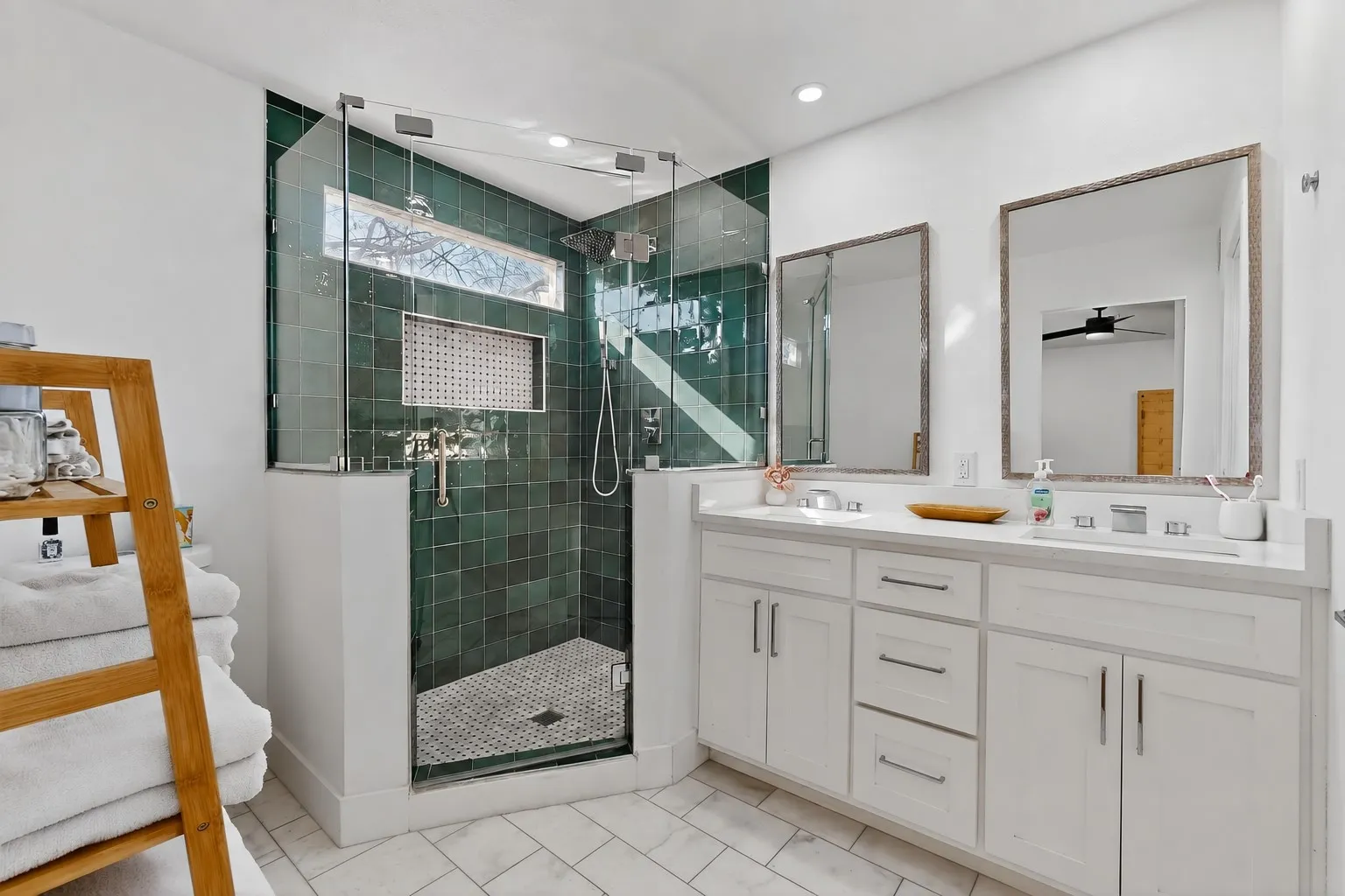 Spacious bathroom featuring a glass-enclosed shower with deep green tile, dual vanity with white cabinetry, and white tile flooring
