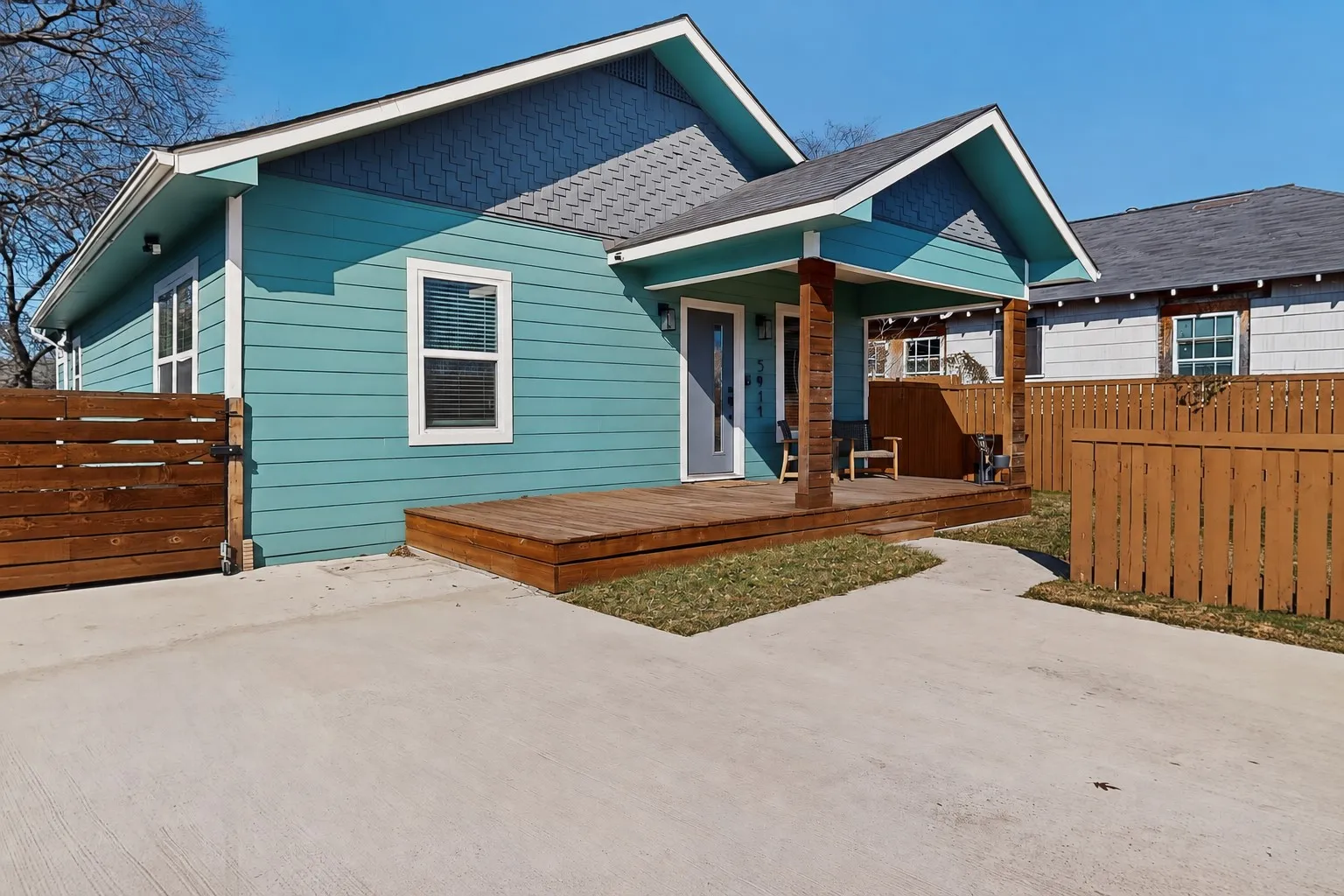 Turquoise siding exterior with white trim, wood-clad porch columns, shingled roofing, and a front porch with a wood deck