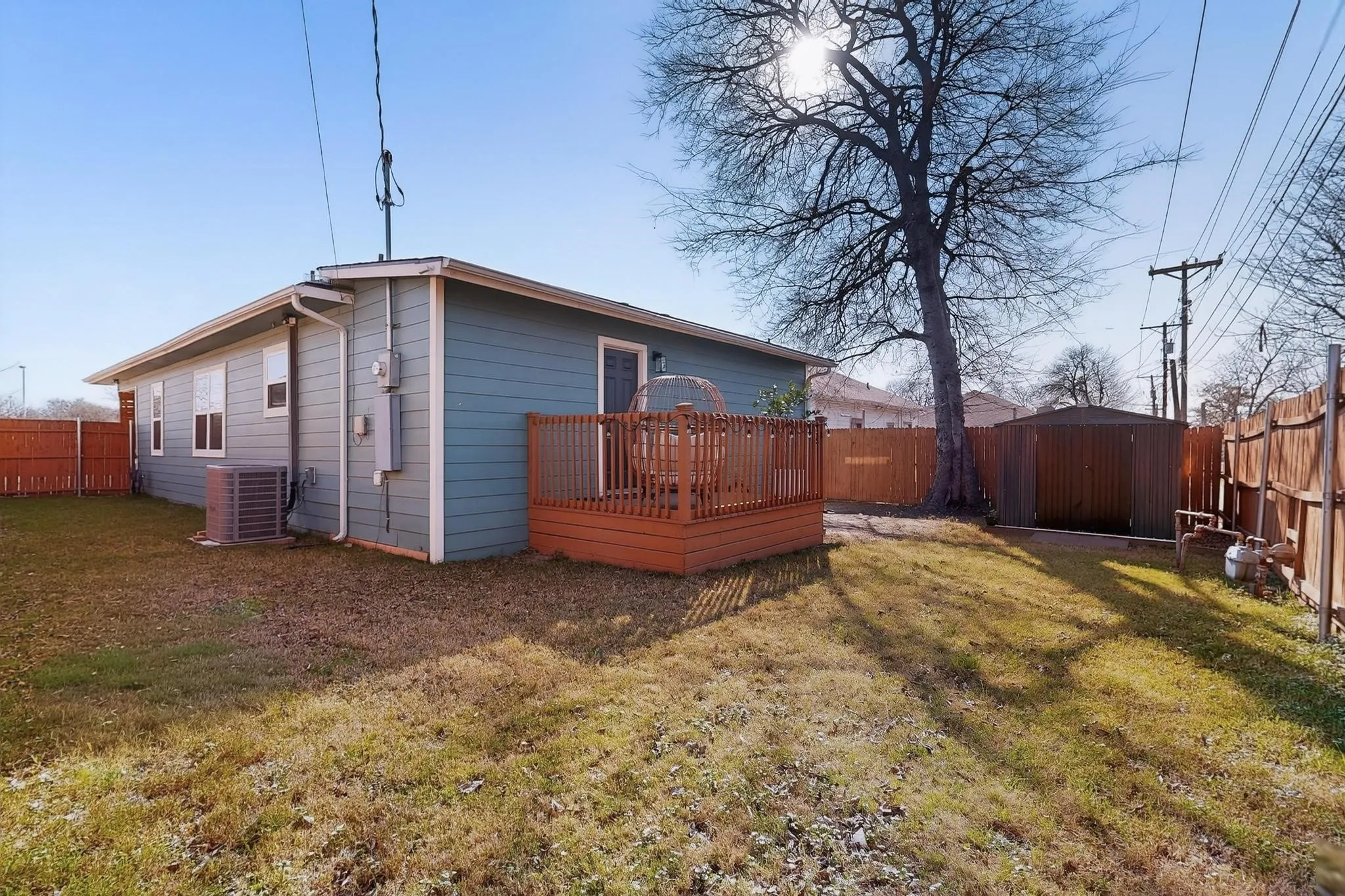 Rear exterior featuring a wood deck, blue siding, fenced yard, and a storage shed