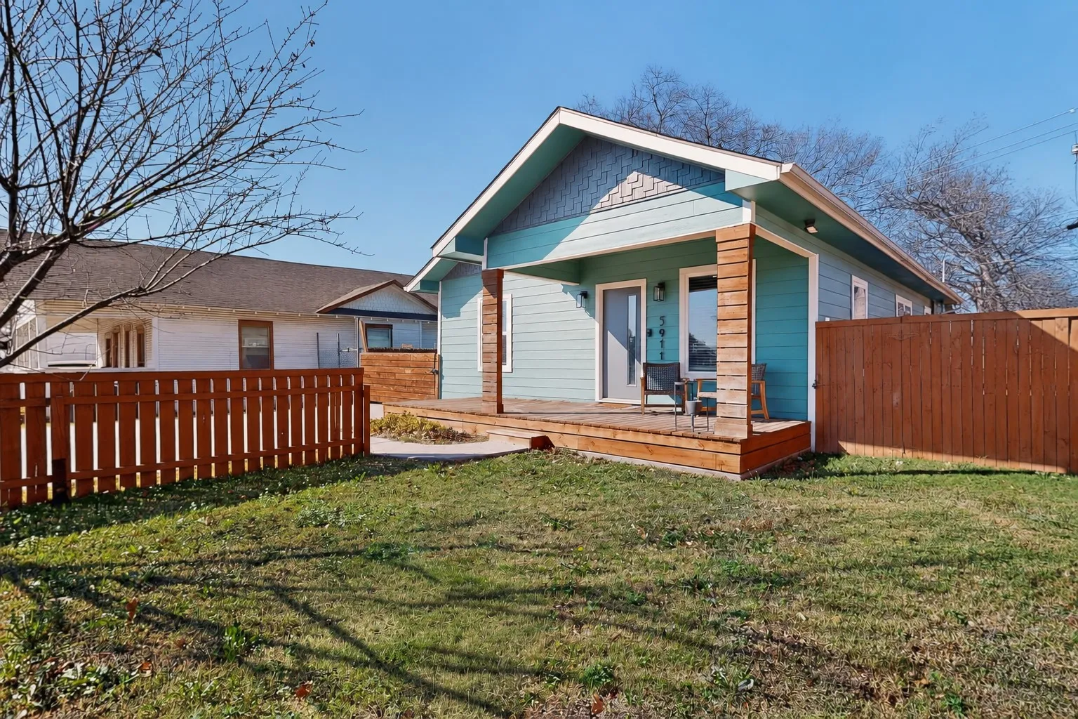Exterior featuring a light blue facade, wood-clad columns, an extended wood porch, a wood privacy fence, and a manicured lawn