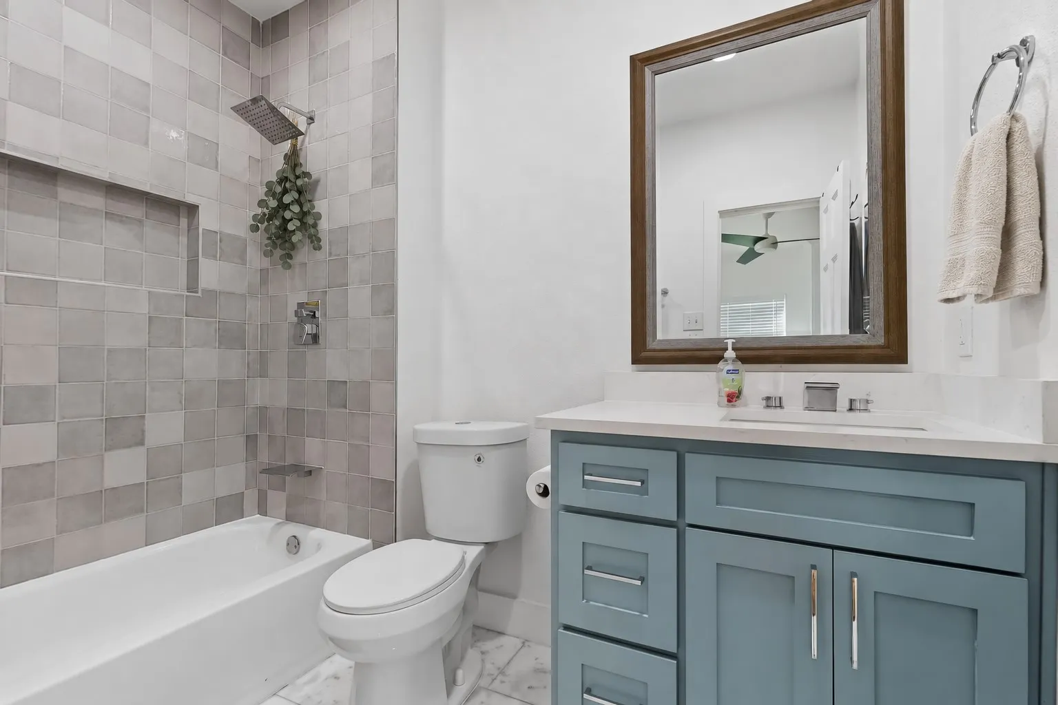 White bathtub with a tiled surround, recessed shower niche, and rain showerhead