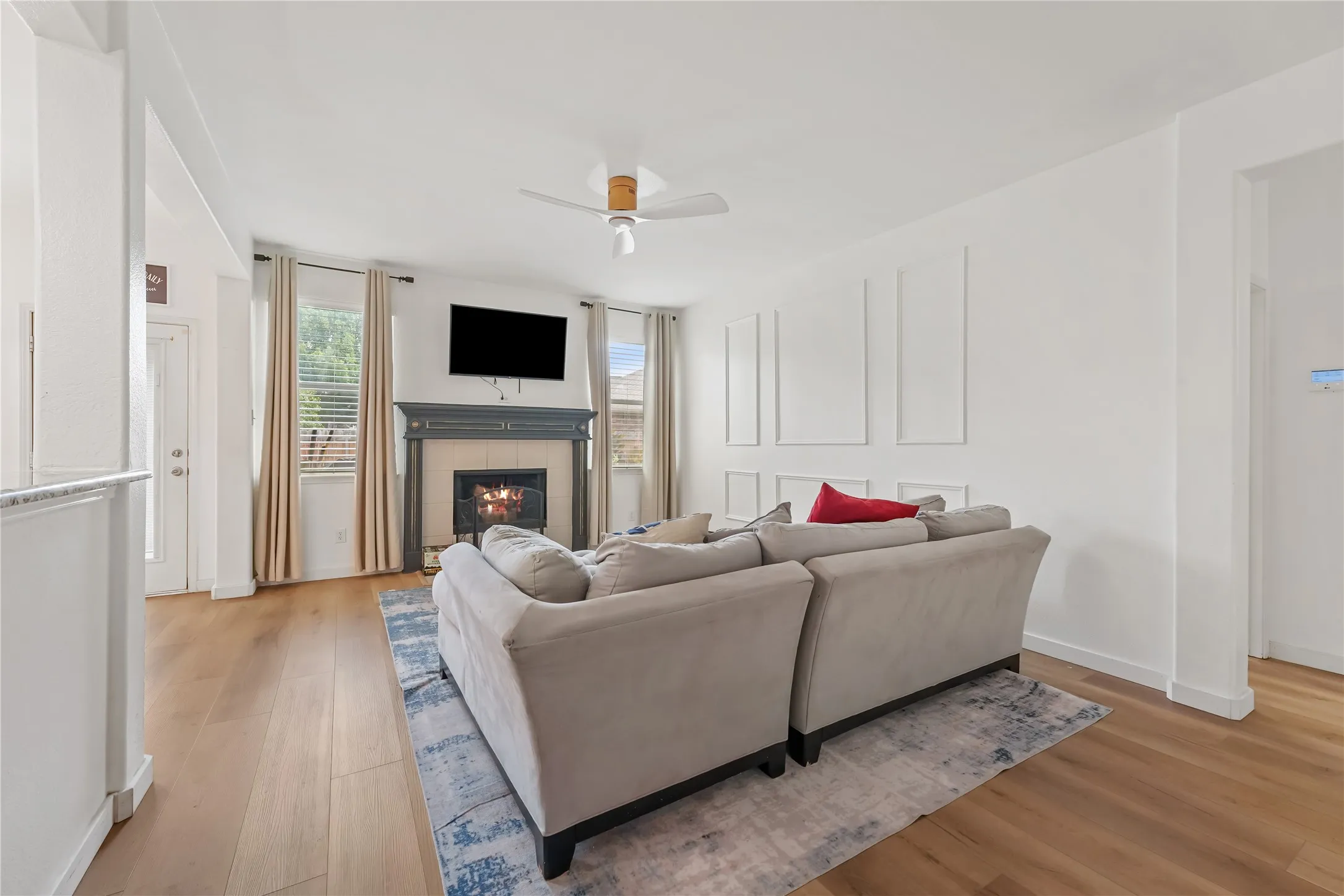 Spacious living area featuring wood-finish flooring, a ceiling fan, and a fireplace with a dark mantel