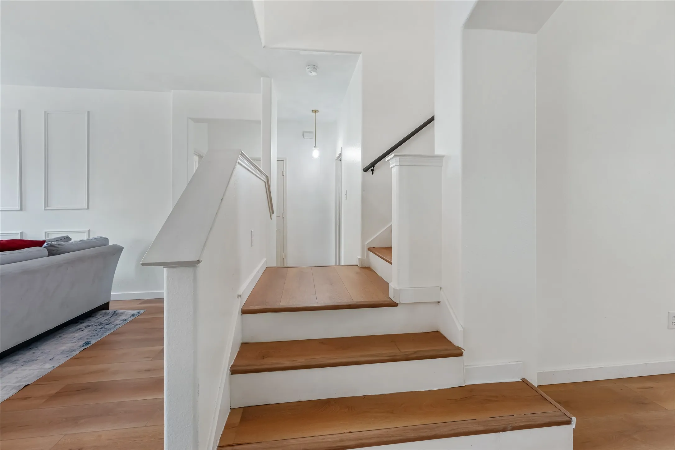 Hardwood stairs with white risers, white wall paneling, and a black handrail