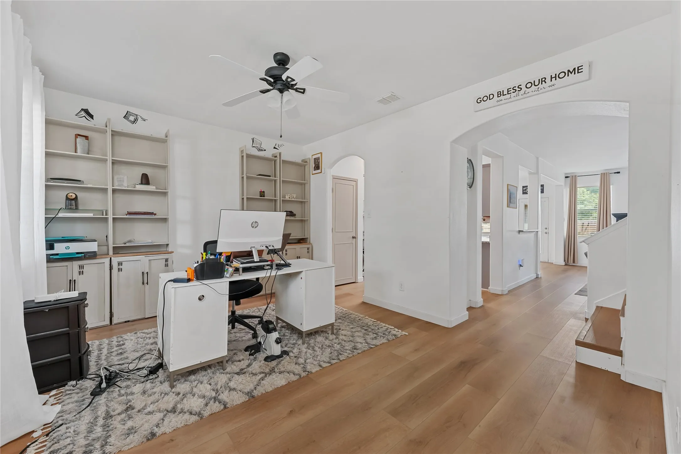 Hardwood-style flooring throughout, integrated ceiling fan, arched doorways, and built-in shelving with lower cabinetry