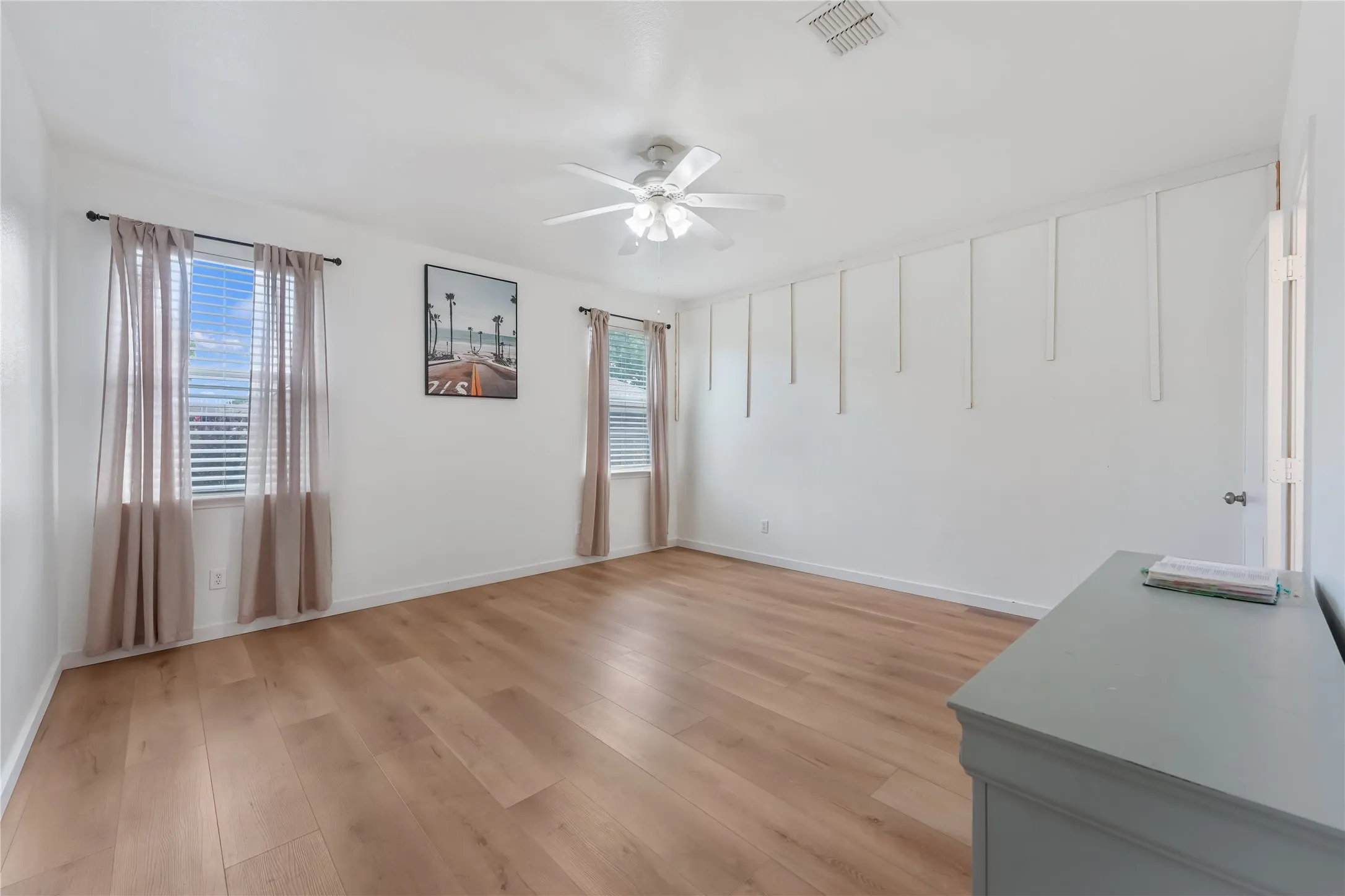 Wood-finish flooring, two windows with blinds, ceiling fan with integrated lighting, and decorative wall molding