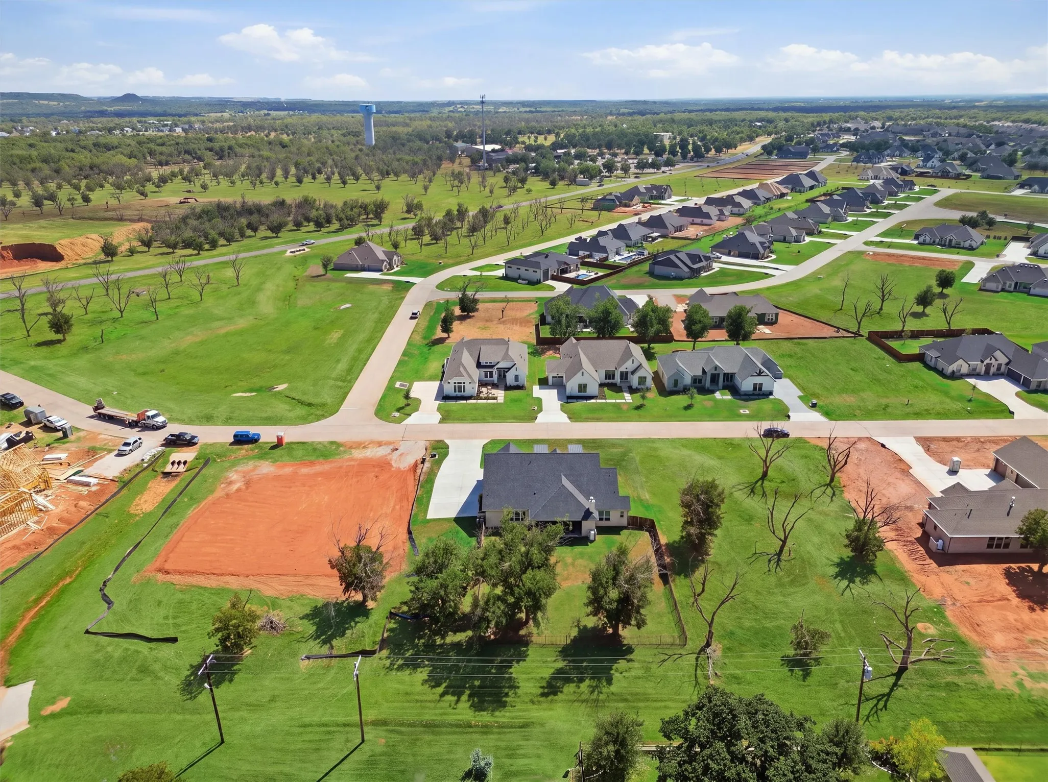 Expansive green spaces surround a newly developed residential area featuring various single-story homes and a visible water tower in the distance