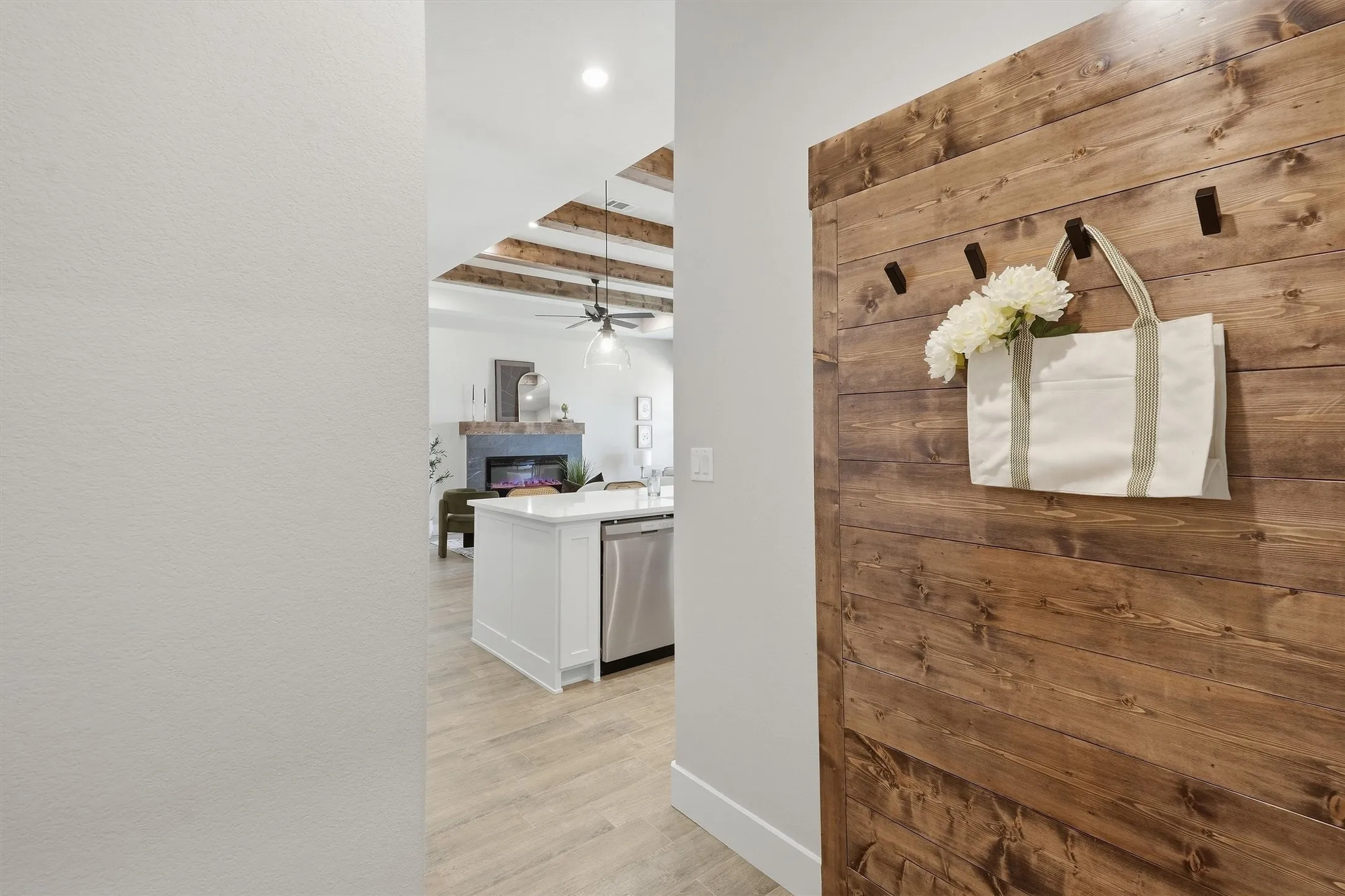 Wood-finish accent wall with integrated hooks, tiled flooring, exposed wood ceiling beams, white kitchen island with integrated stainless steel appliance, and a built-in fireplace