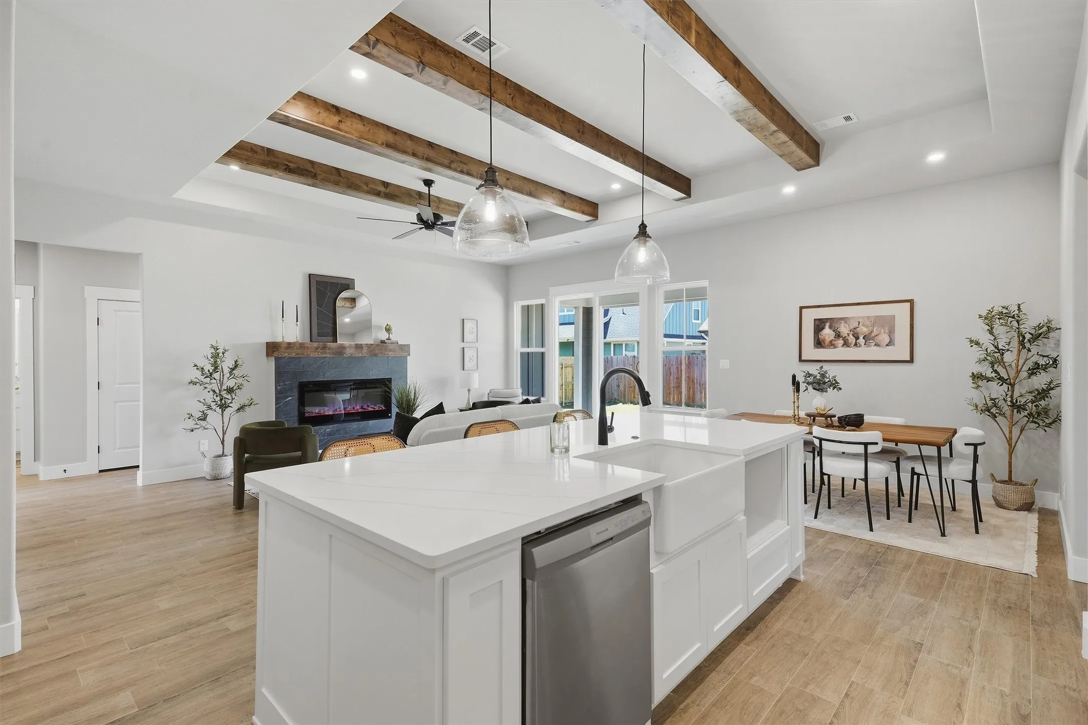 Kitchen island with a white countertop and integrated sink, exposed beam ceiling, recessed lighting, and a built-in fireplace with a stone surround