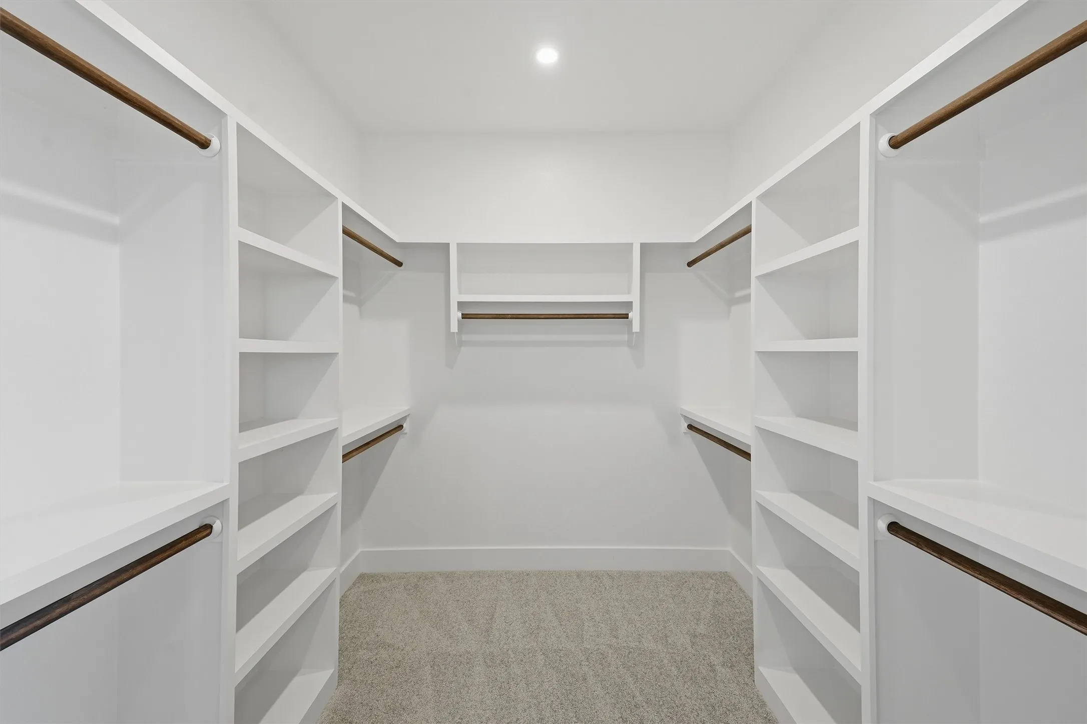 Built-in shelving, white cabinetry, integrated hanging rods, recessed lighting, and carpeted flooring